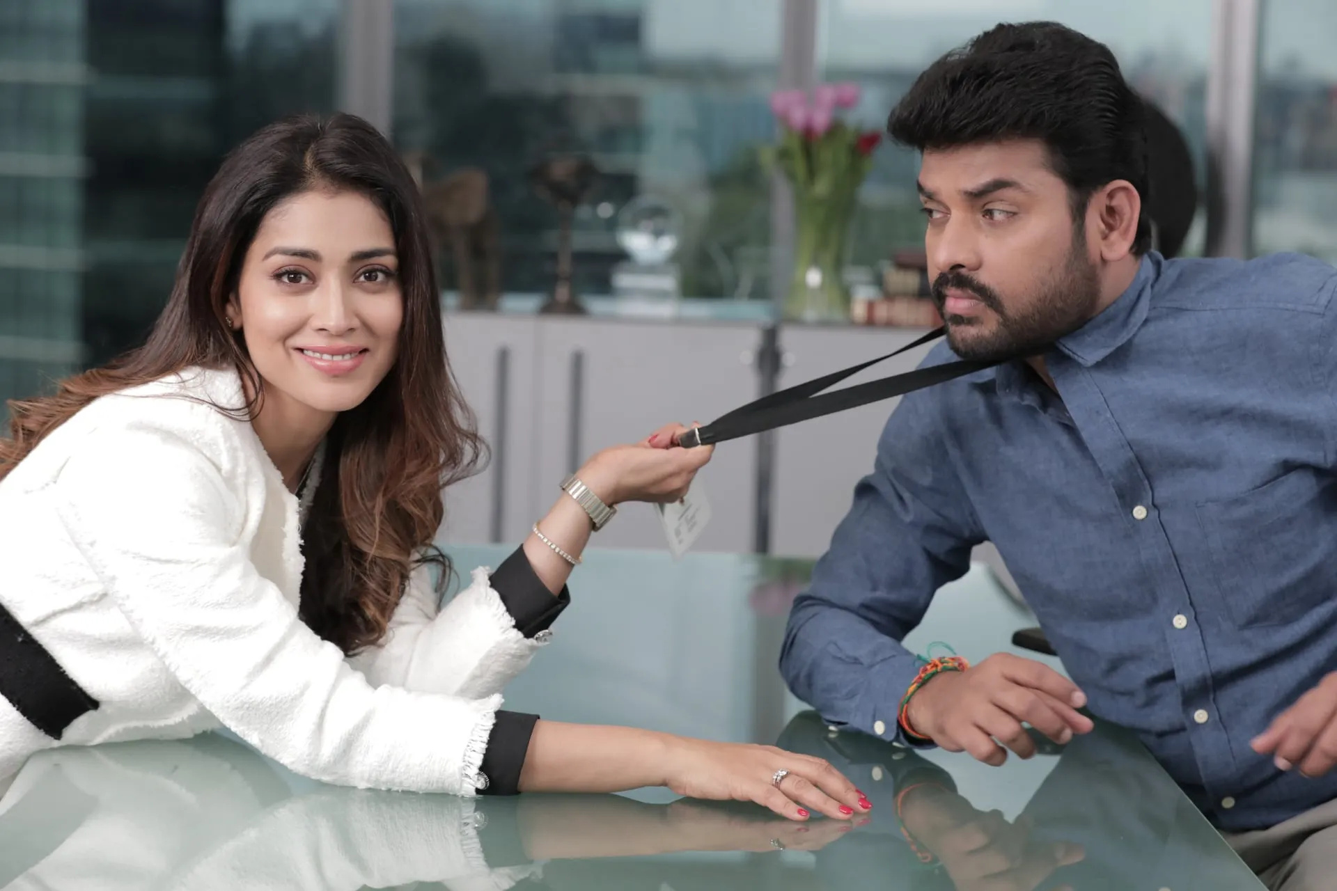 Shriya Saran leans across an office desk and tugs Vimal towards her by his ID lanyard in a still from Sandakkari