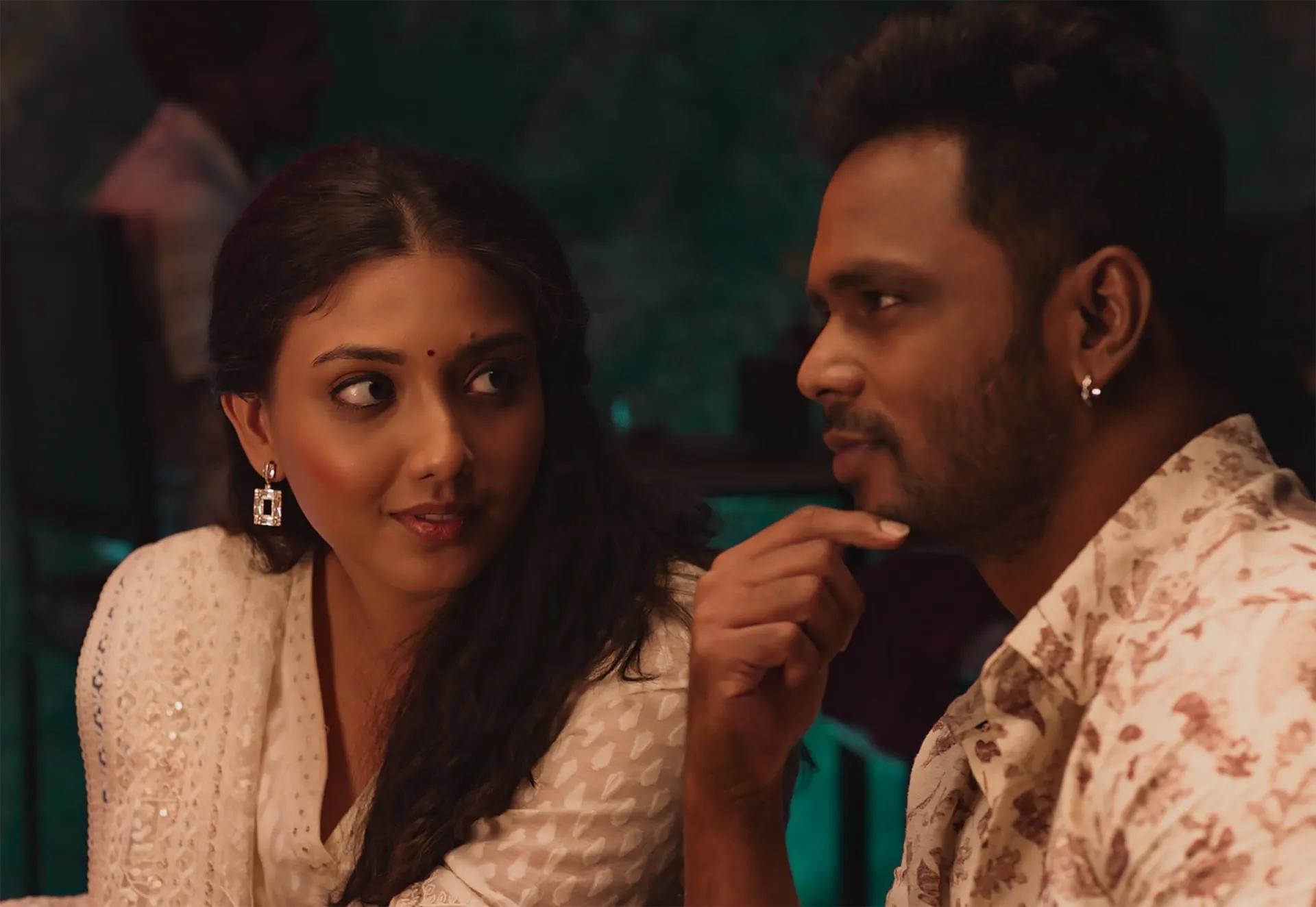 A couple leaning close in conversation at a dimly lit table in a still from Yen Ennai Yetho Seithai