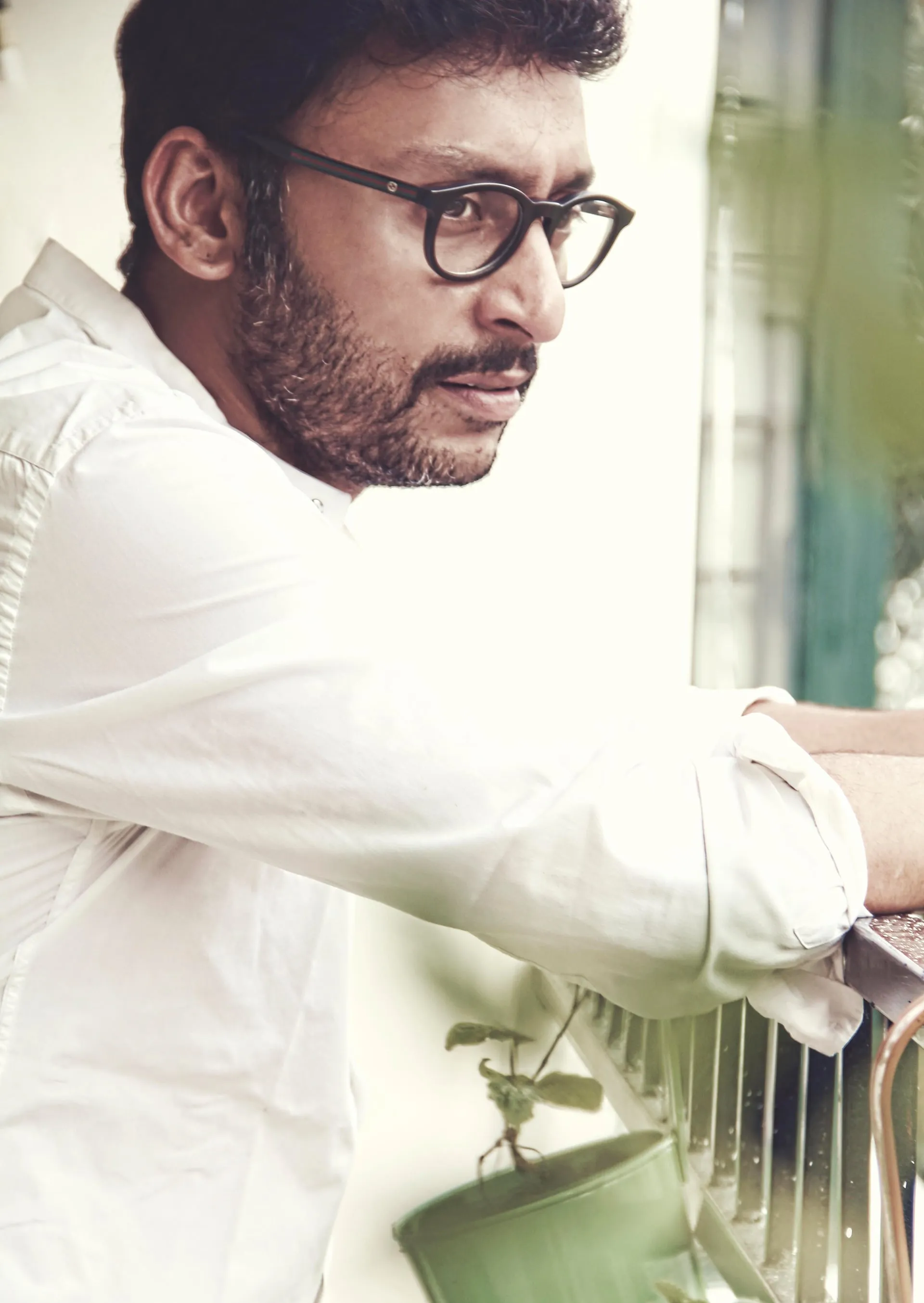 RJ Balaji in a portrait, leaning on a balcony rail in a white shirt and dark-rimmed glasses