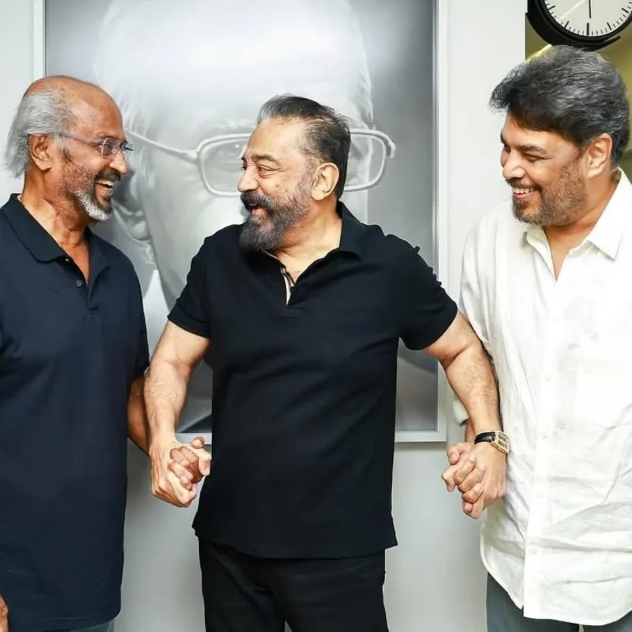 Rajinikanth, Kamal Haasan and Sundar C laughing together, hands clasped, in front of a portrait