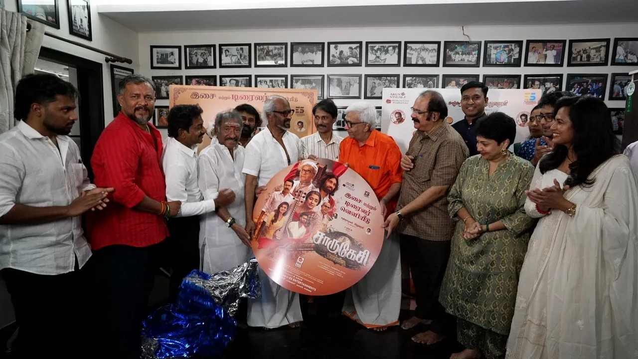 Rajinikanth standing centre with Y Gee Mahendra and the Charukesi team, holding the film's audio album disc against a wall of framed black-and-white production stills