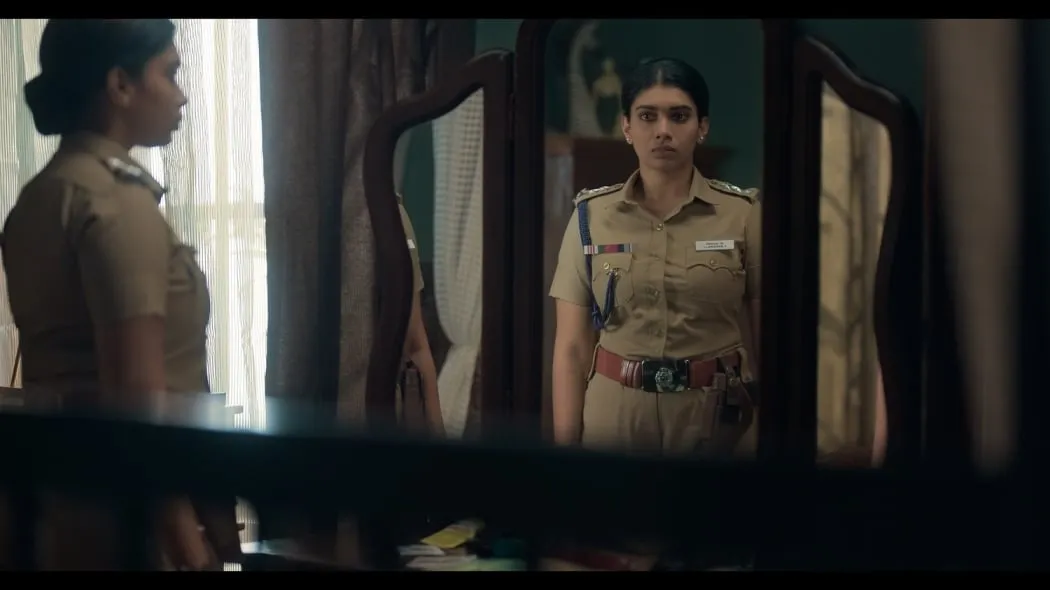 Police officer in khaki uniform standing in front of a dressing-table mirror in a still from Prime Video's Tamil suspense series Exam, premiering May 15.