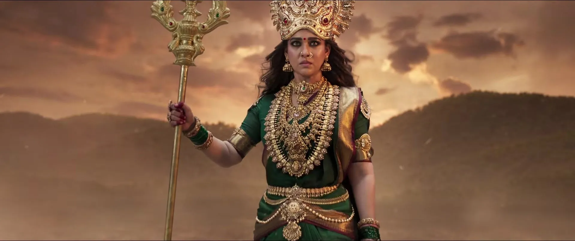 Nayanthara as the goddess Mookuthi Amman, crowned and holding a golden trident against a dusky sky