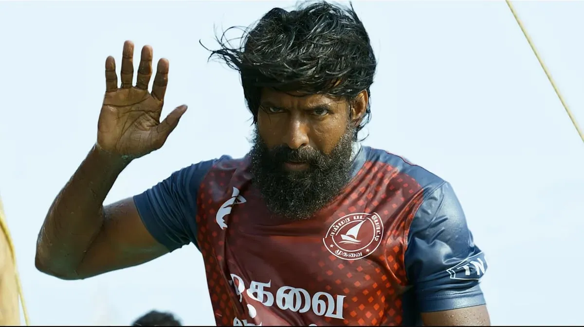 Soori as Muthukaali in Mandaadi, bearded and in a boat-crew racing jersey, raising one hand with the sea behind him