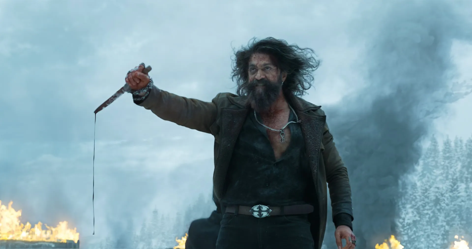 Yash as Raya holding out a dripping blade amid snow, smoke and flames in Toxic