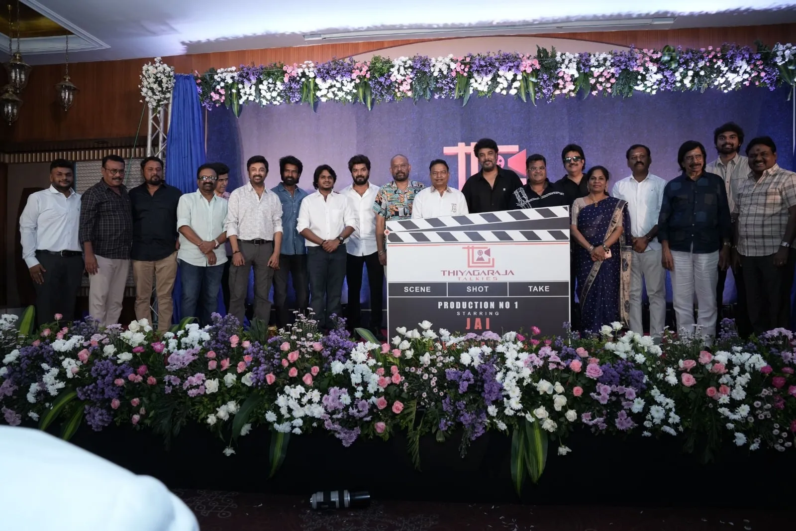 Guests stand on stage behind the Thiyagaraja Talkies Production No 1 clapboard