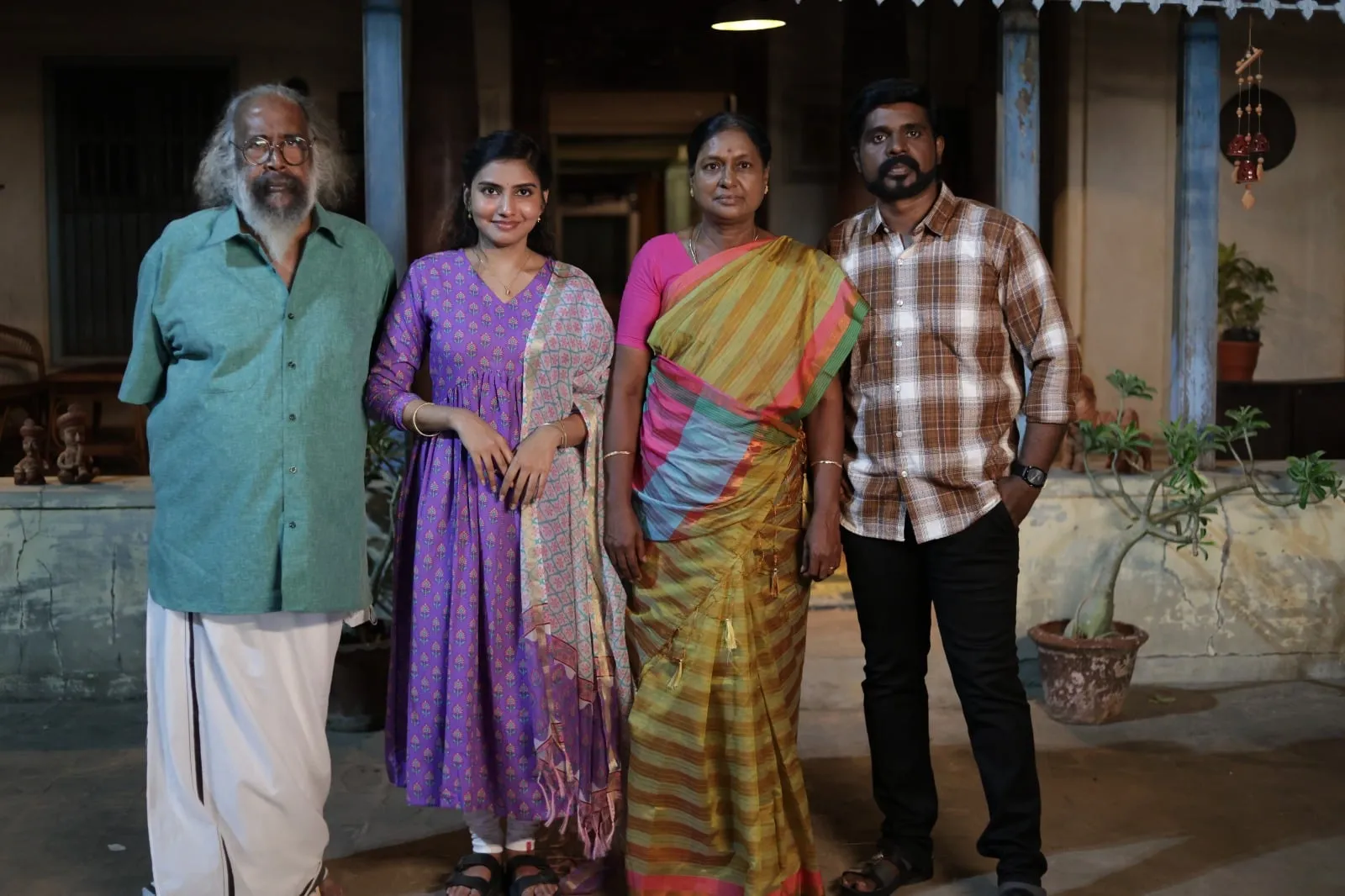 Four members of the Dhrogam Pazhagu cast stand together outside a house in a film still