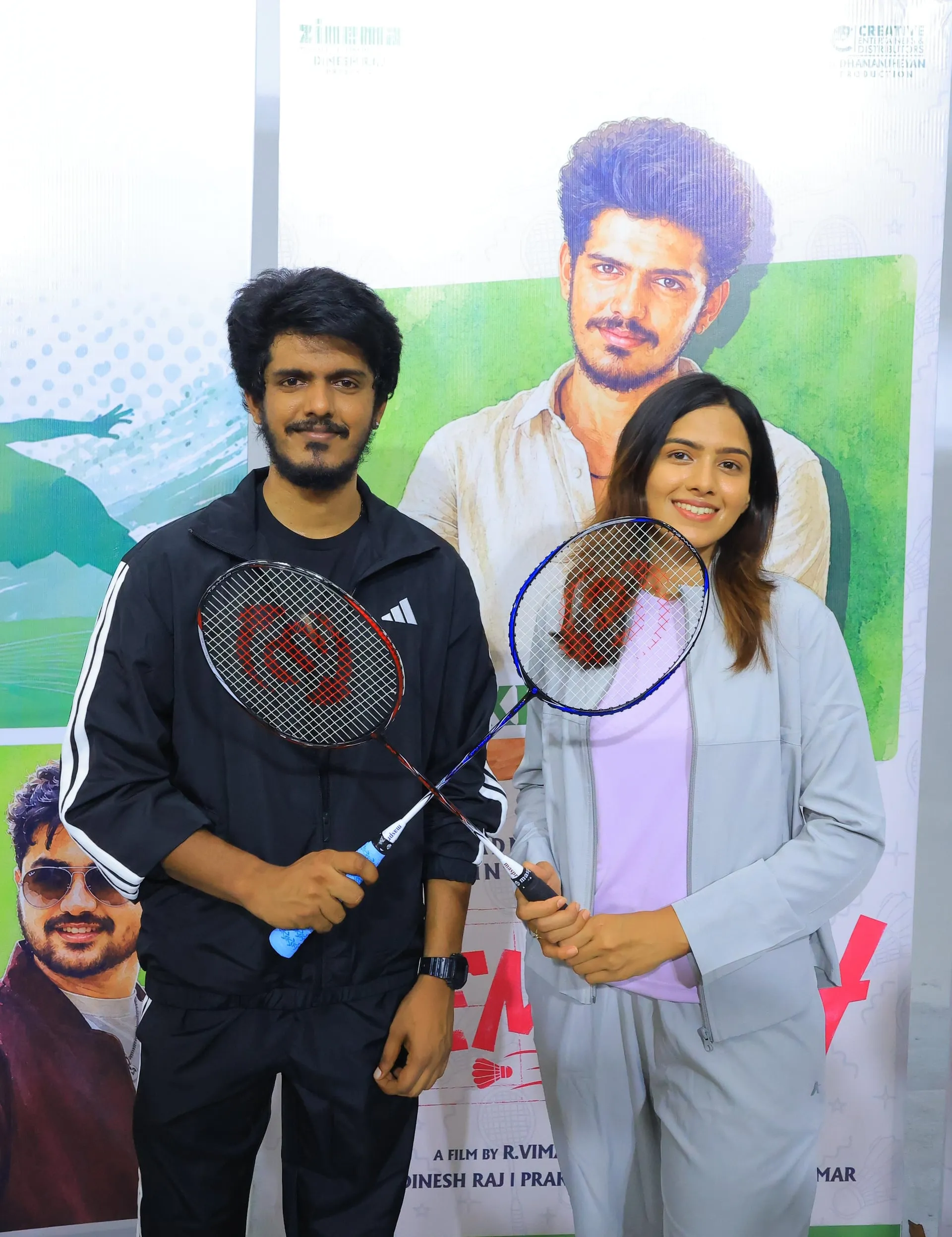 KPY Bala and Dhanu Harsha holding badminton rackets in front of the Rematch poster