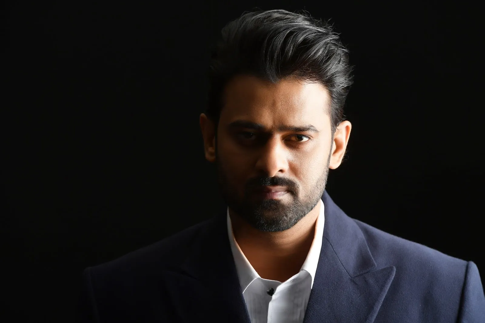 Prabhas in a dark suit against a black background
