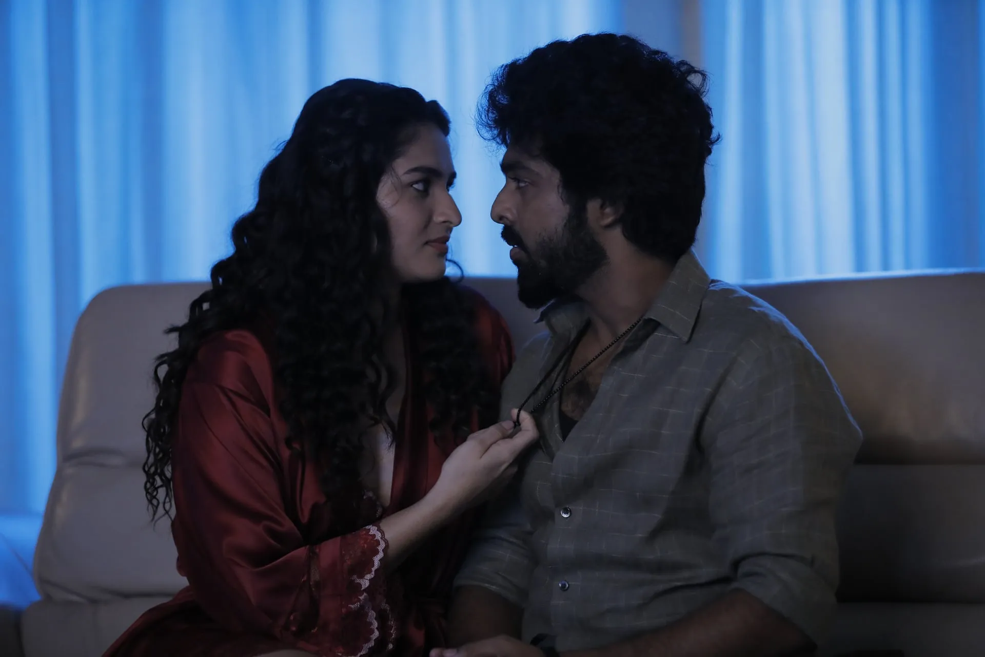 Kayadu Lohar as Sindhu in a red satin robe on a couch beside GV Prakash Kumar as Magi, her hand at his collar, in a blue-lit room in Immortal