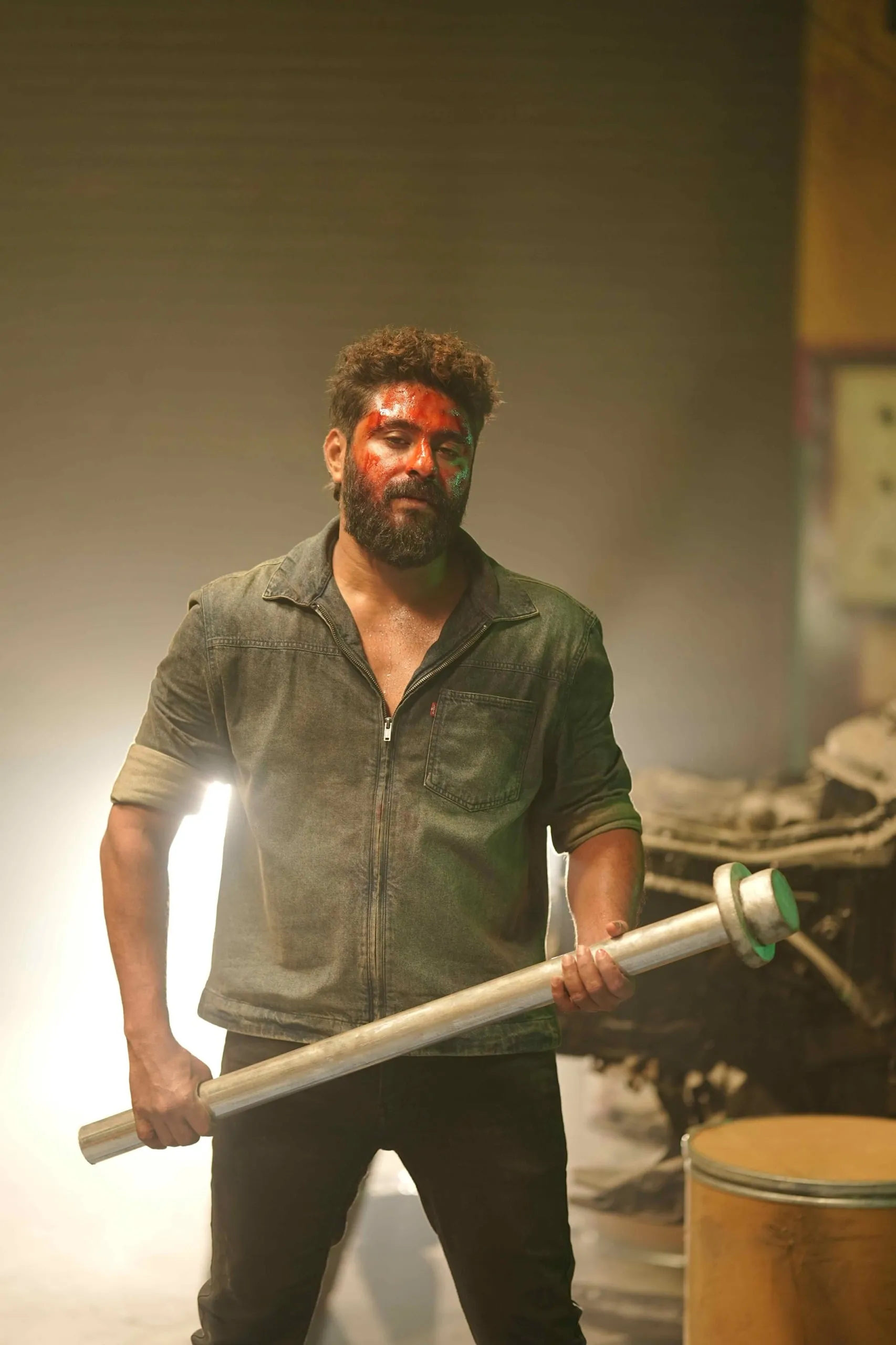 Antony Varghese, face streaked with red, gripping a metal pole in a smoke-filled garage in Kattalan