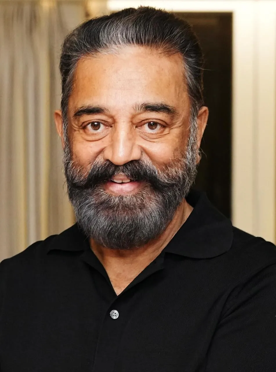 Kamal Haasan in a black polo, head-and-shoulders portrait, smiling slightly with a soft cream backdrop