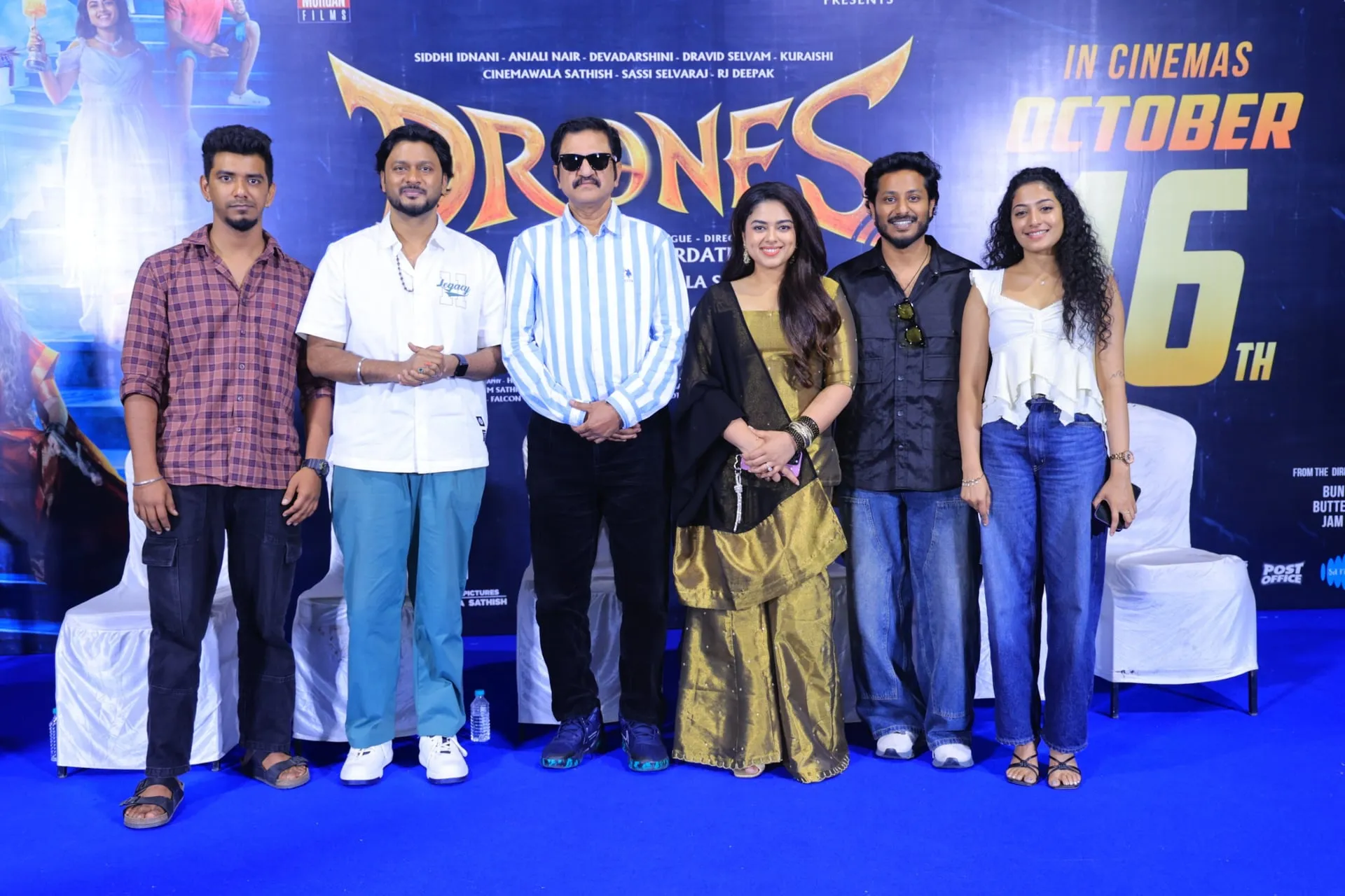Producer GM Morgan with Siddhi Idnani, Anjali Nair, Dravid Selvam, Cinemawala Sathish and RJ Deepak in front of the Drones release poster