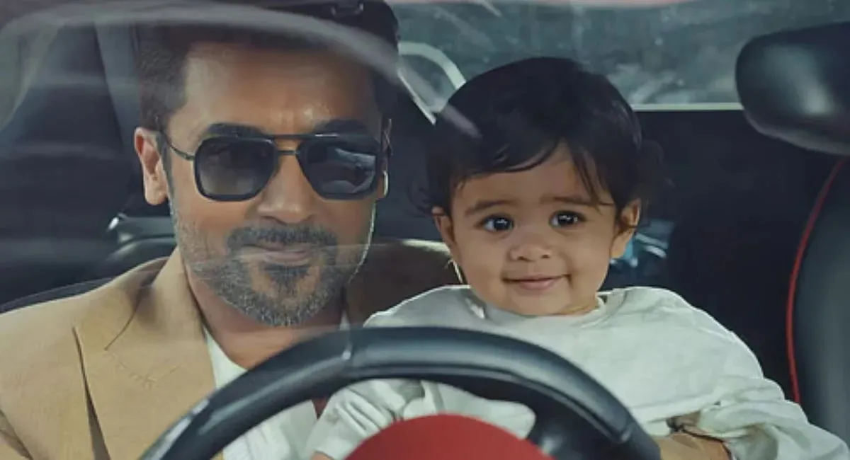 Suriya as Sanjay Vishwanath smiles behind the wheel with a baby on his lap in a still from Vishwanath & Sons