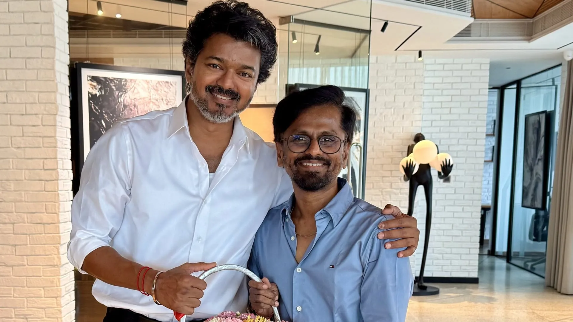 Vijay in a white shirt with his arm around director AR Murugadoss, both smiling in a bright room
