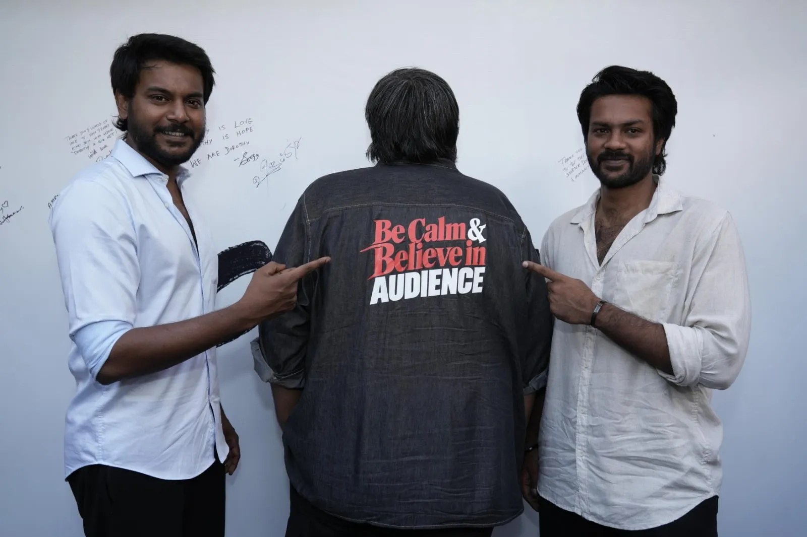 Two men point at the back of a jacket printed with Be Calm and Believe in Audience at the Dorothy thanksgiving event