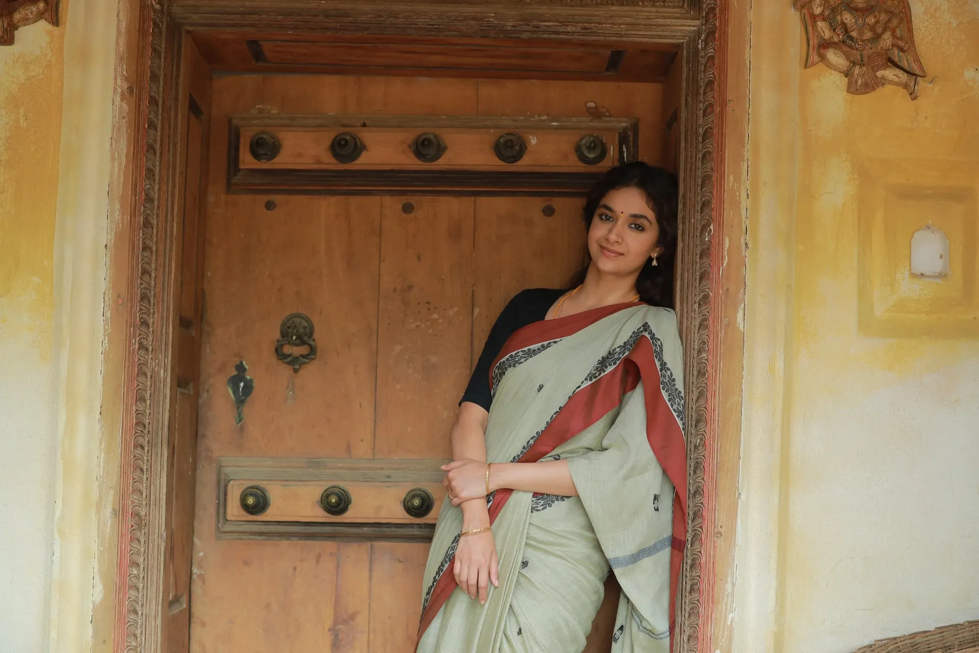 Keerthy Suresh stands beside a carved wooden doorway in Dorothy.