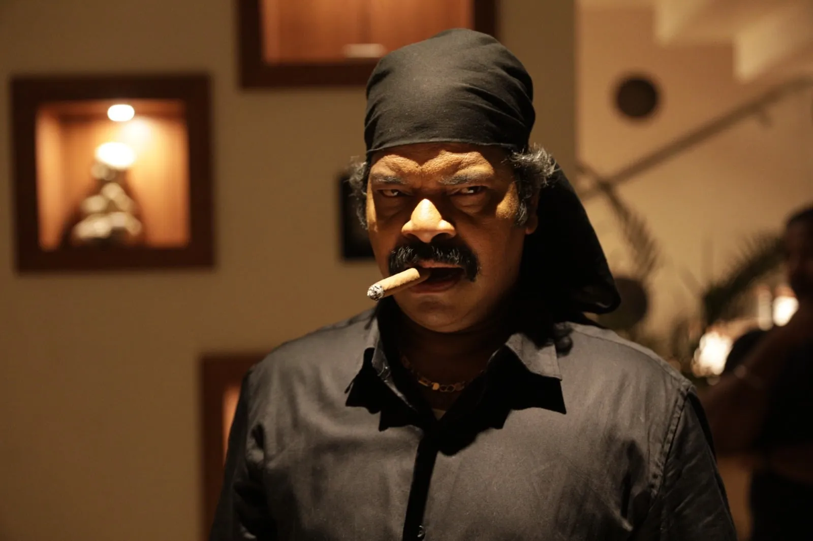 Ravi Mariya as the watchman in 4 Idiots, in a black bandana and black shirt with a cigar in his mouth