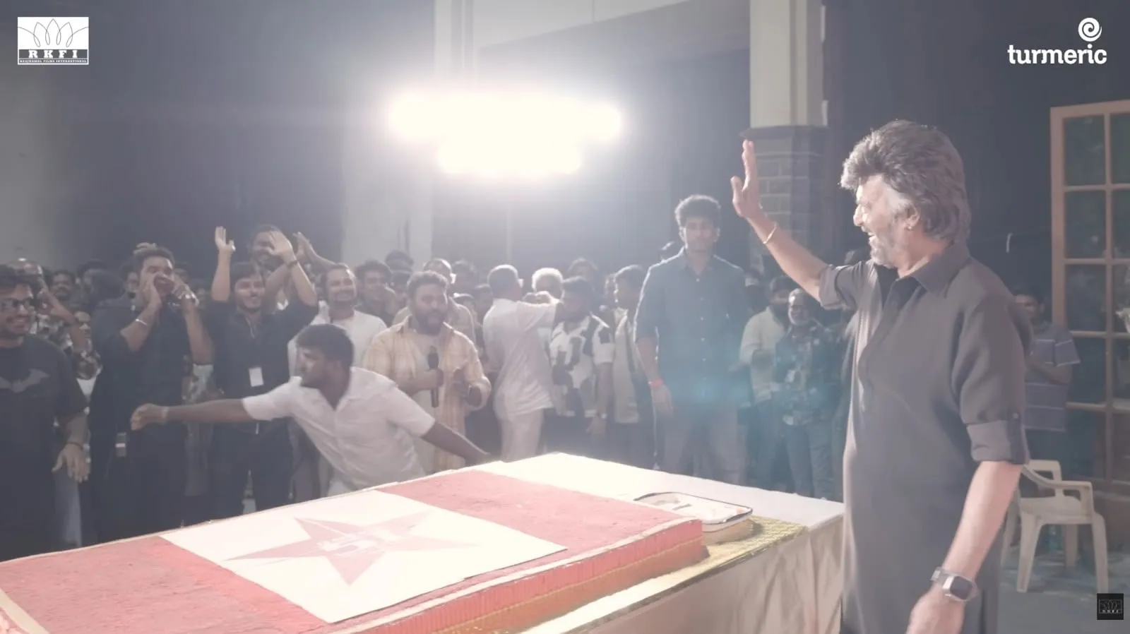 Rajinikanth waves to the cheering Dharman crew across the celebration cake