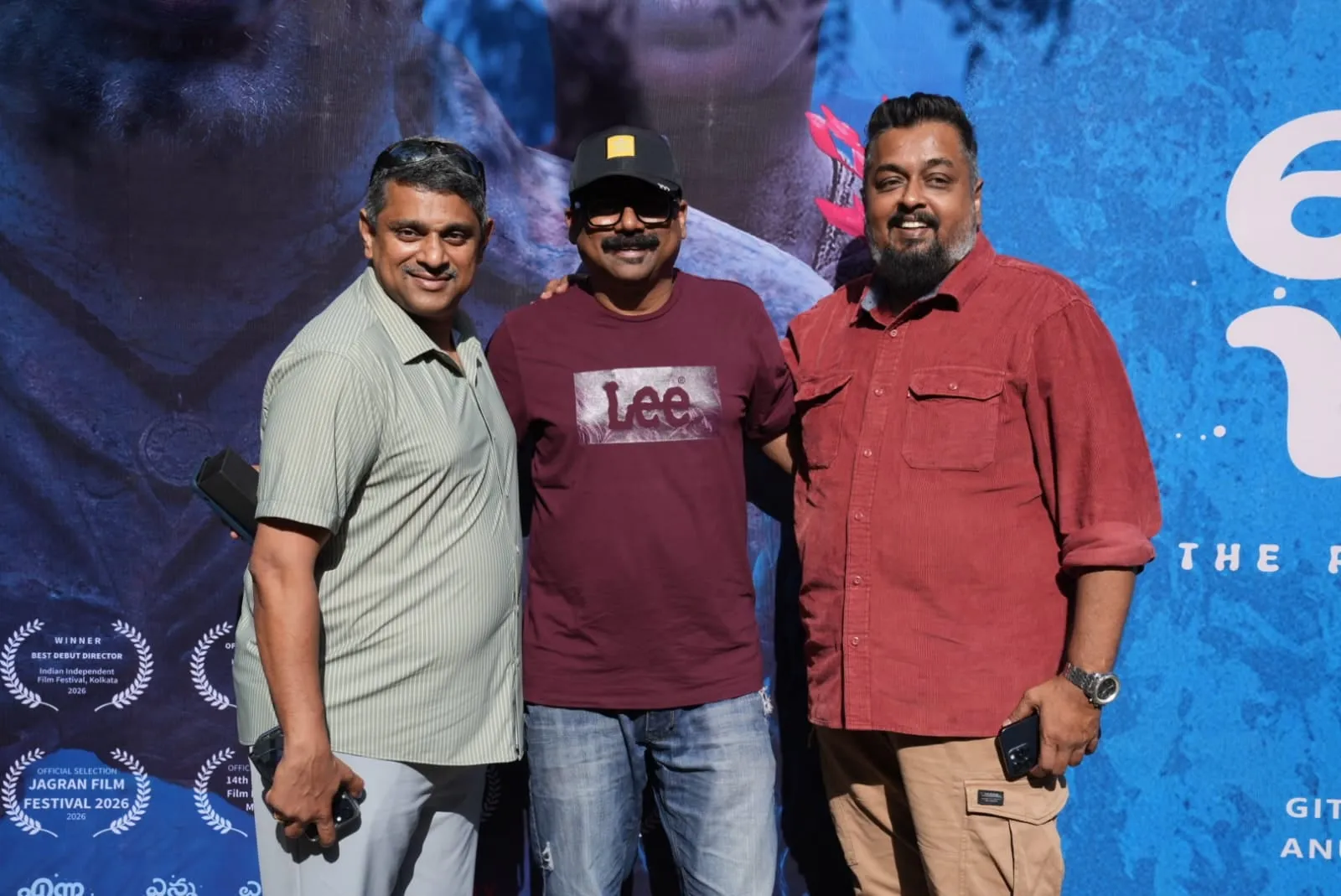 Three members of the Enna Vilai team pose together before the film's blue trailer-launch backdrop