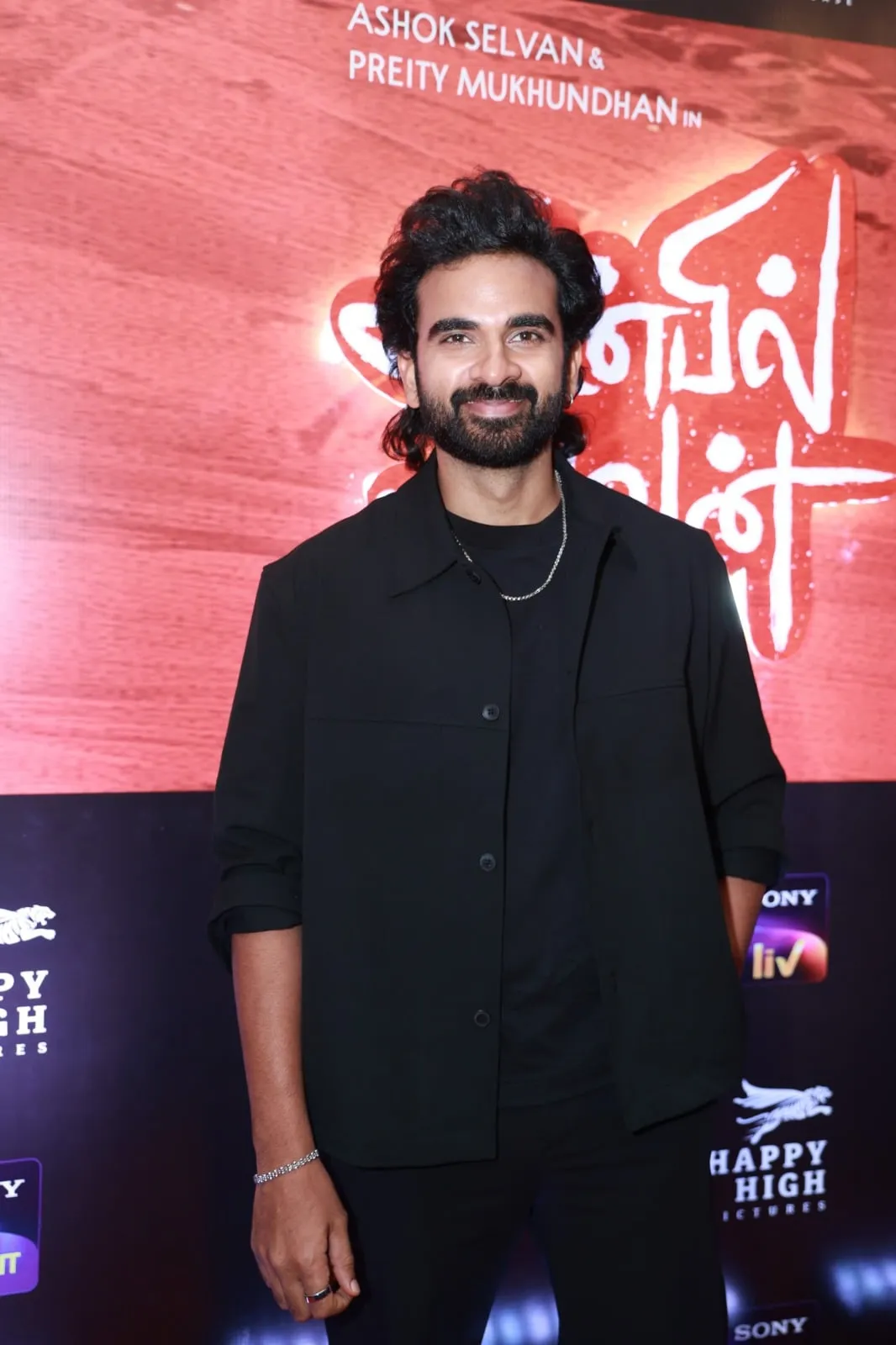 Portrait in a black jacket against Anbil Avan's red event backdrop