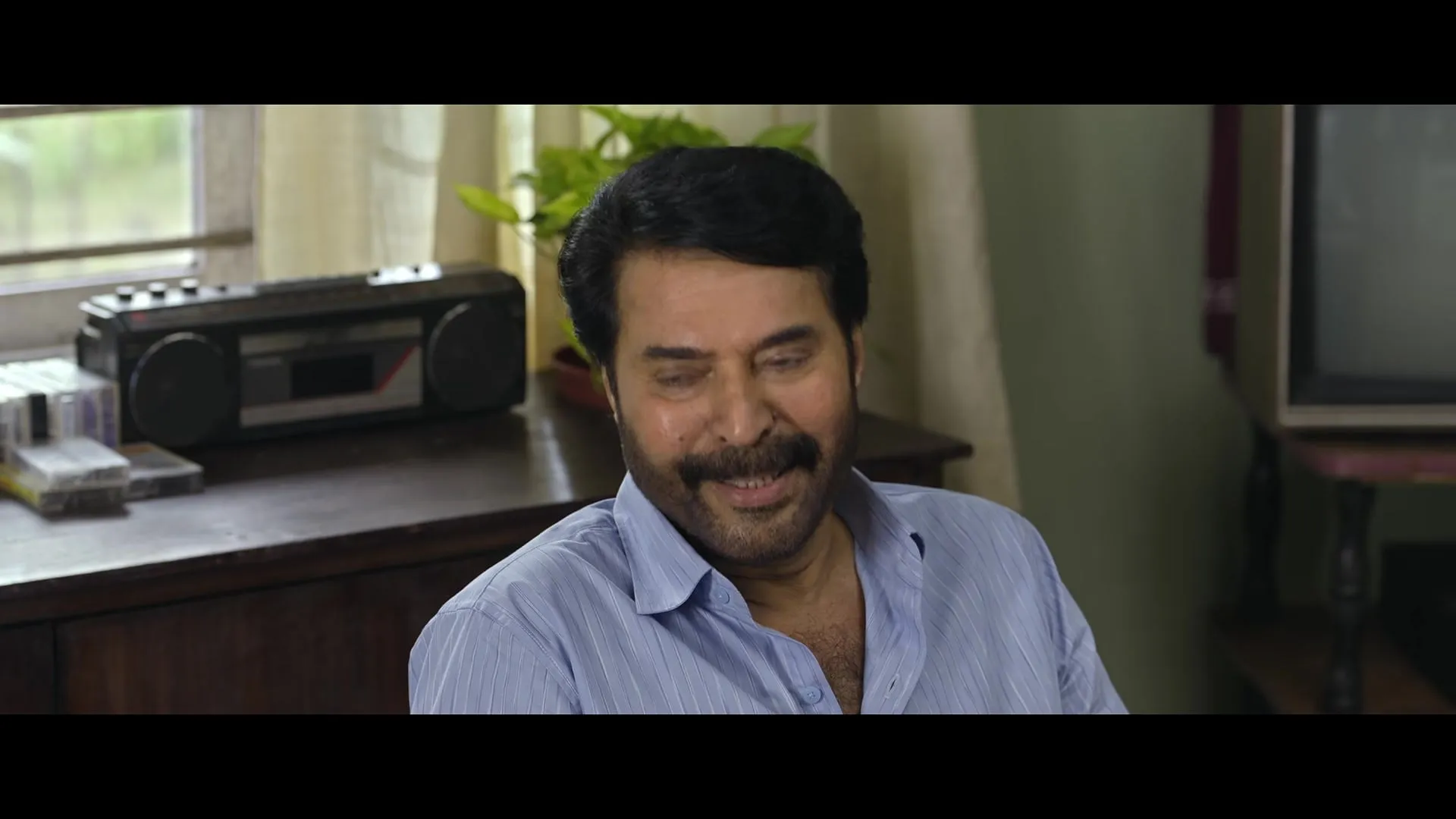 Mammootty smiles at a desk beside an old cassette player in a scene from the Padayaatra trailer