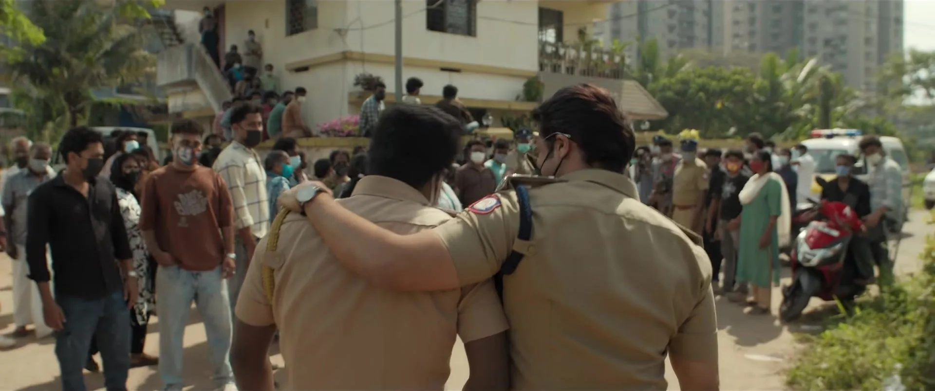 A police officer and a man walk arm in arm through a crowd outside a station in the Scene teaser
