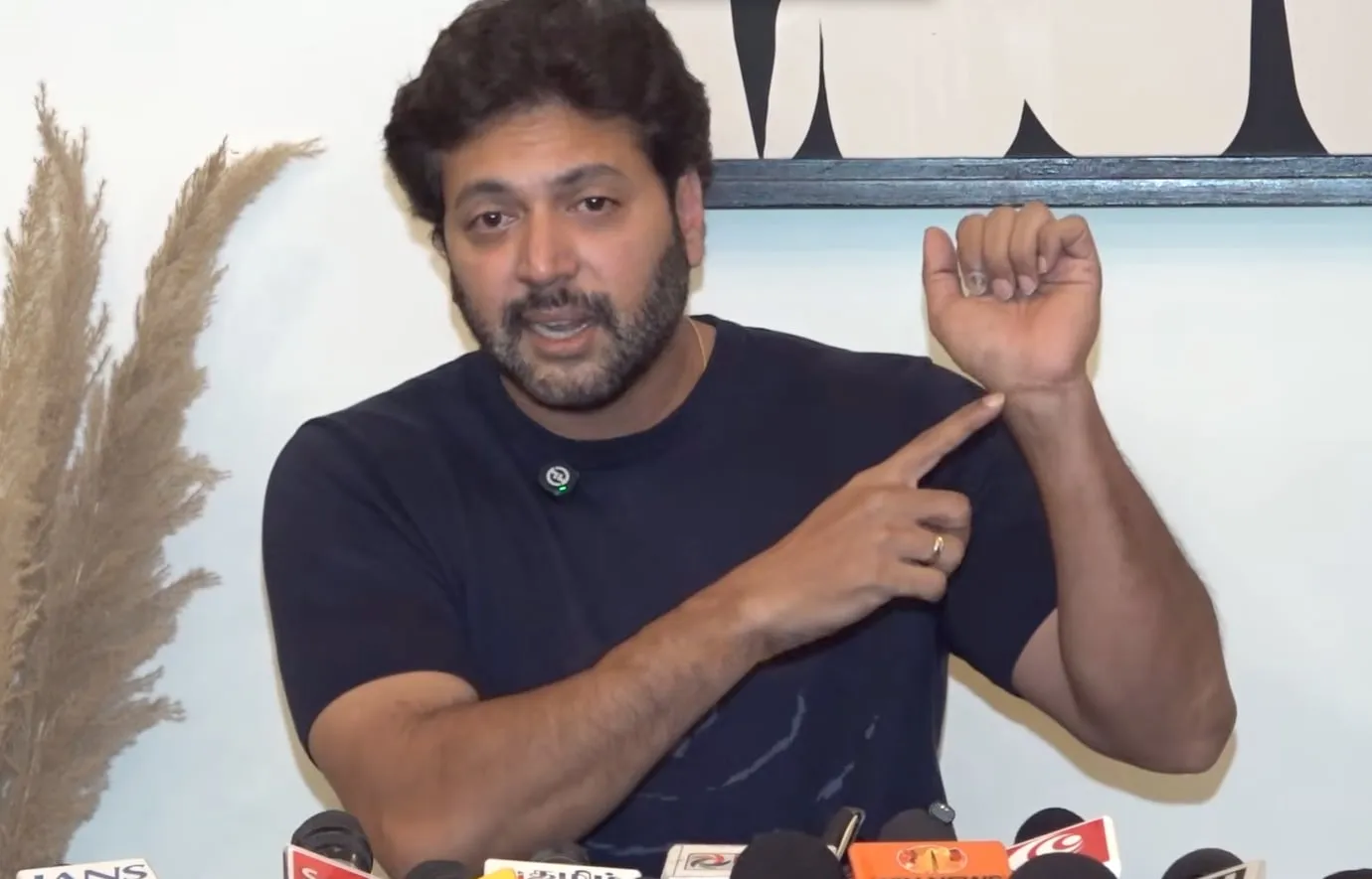 Ravi Mohan pointing to his wrist as he tells reporters he has started hurting himself