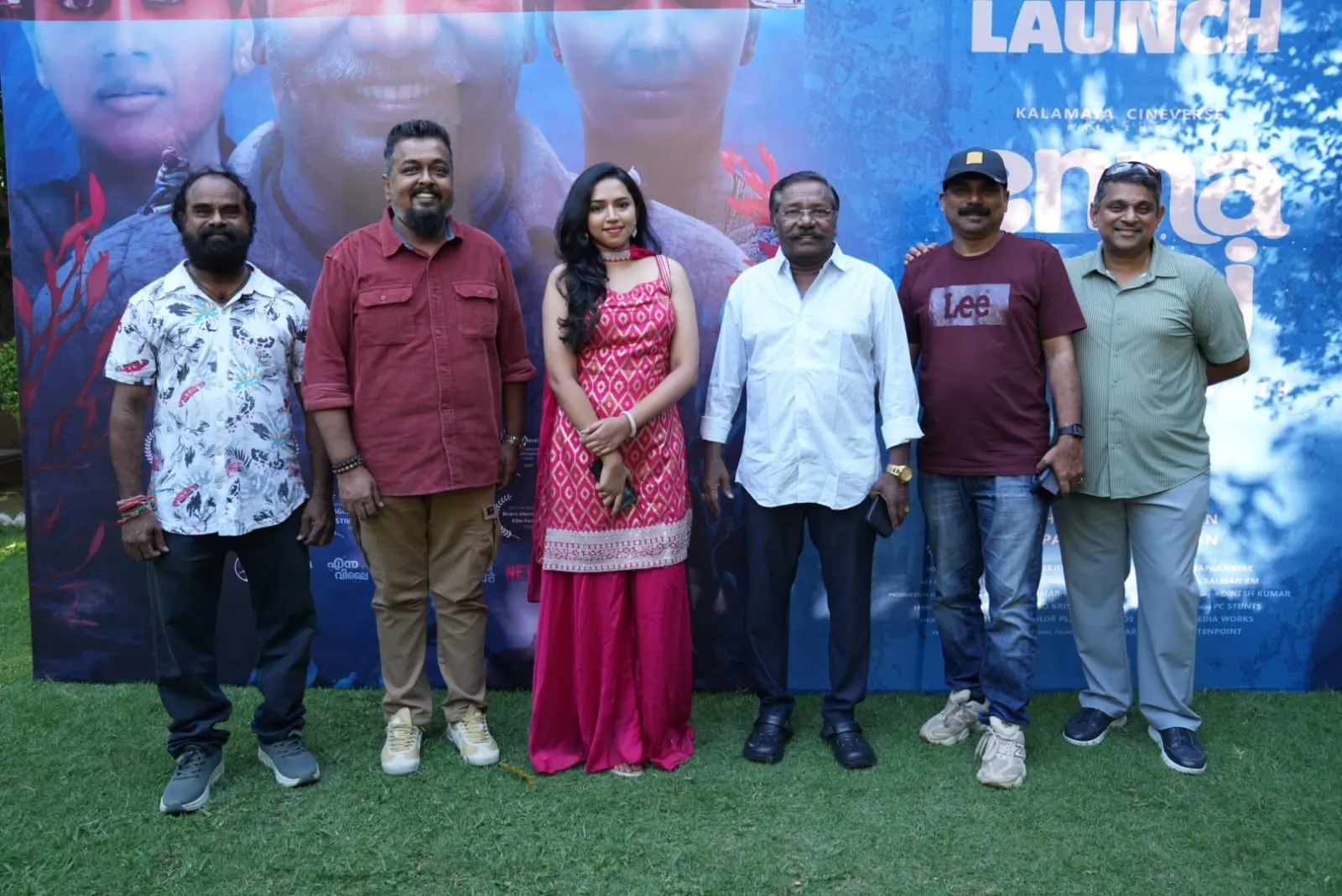 Six members of the Enna Vilai team stand together in front of the film's trailer artwork