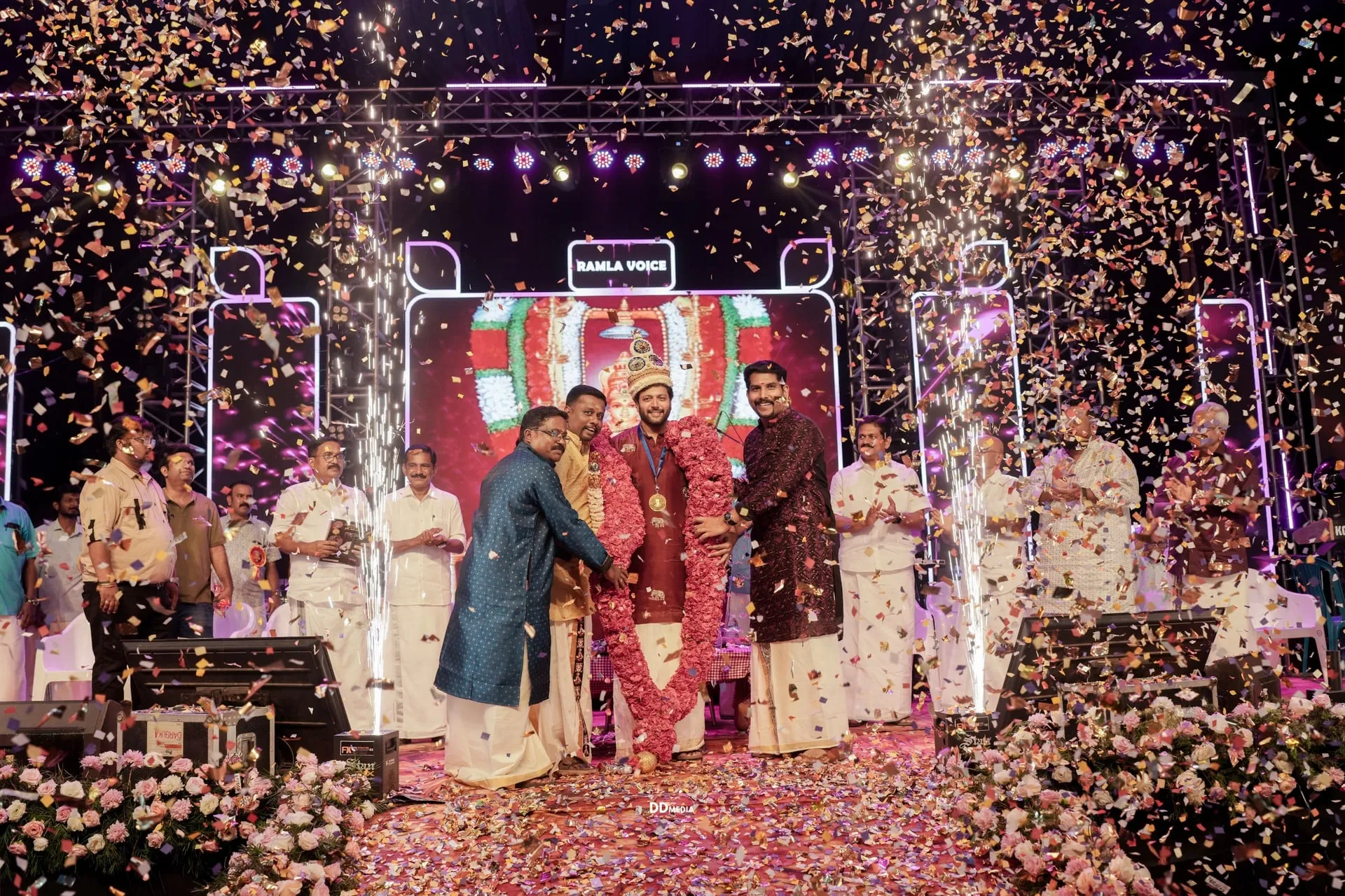 Ravi Mohan on stage with the trophy as flower-petals and sparklers come down, flanked by the trustees who instituted the award.