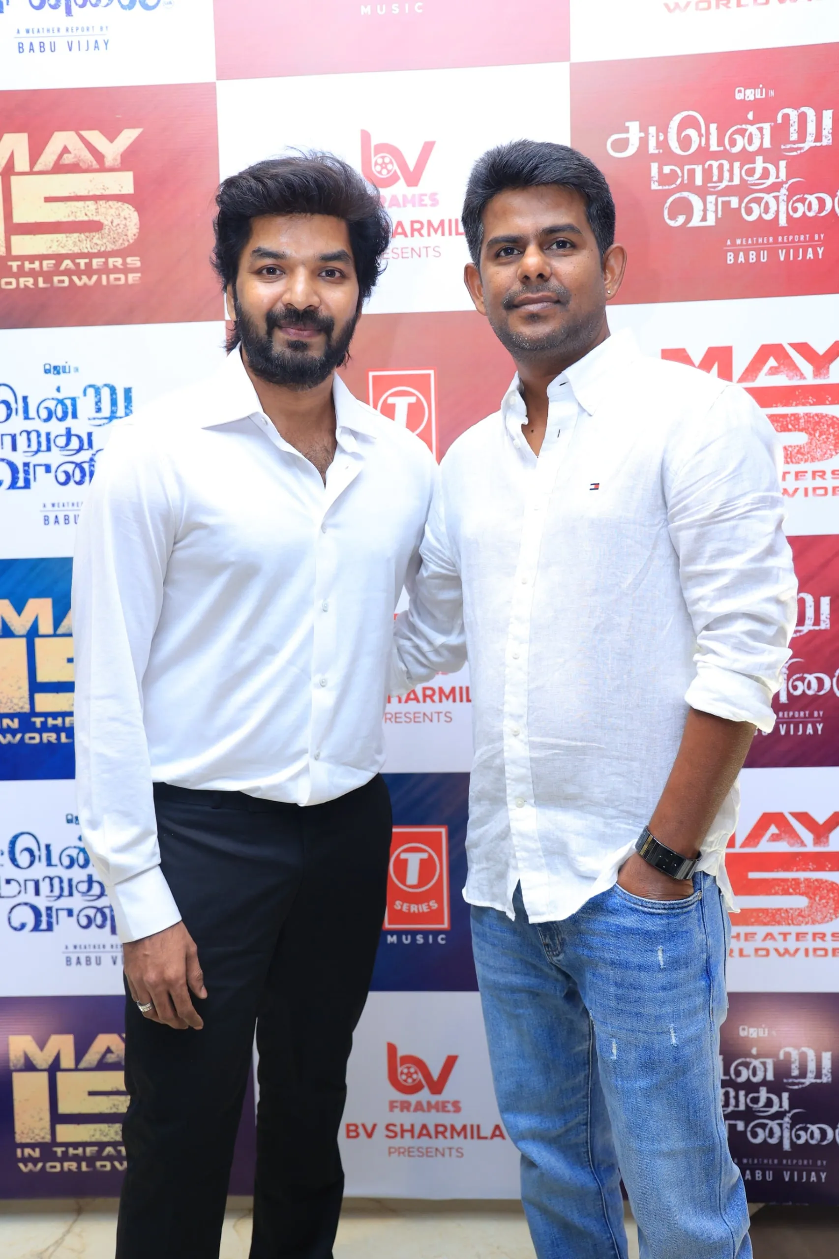 Jai with director Babu Vijay. The white-shirt-and-black-trousers turnout mirrors the palette Joseph Vijay wore at his swearing-in two days earlier; the visual cue is not subtle.