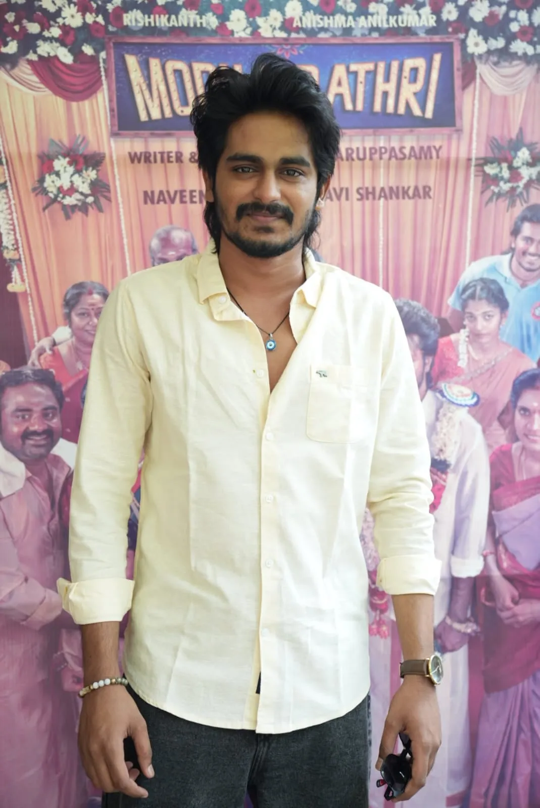 A guest in a pale yellow shirt poses in front of the film's wedding-themed backdrop