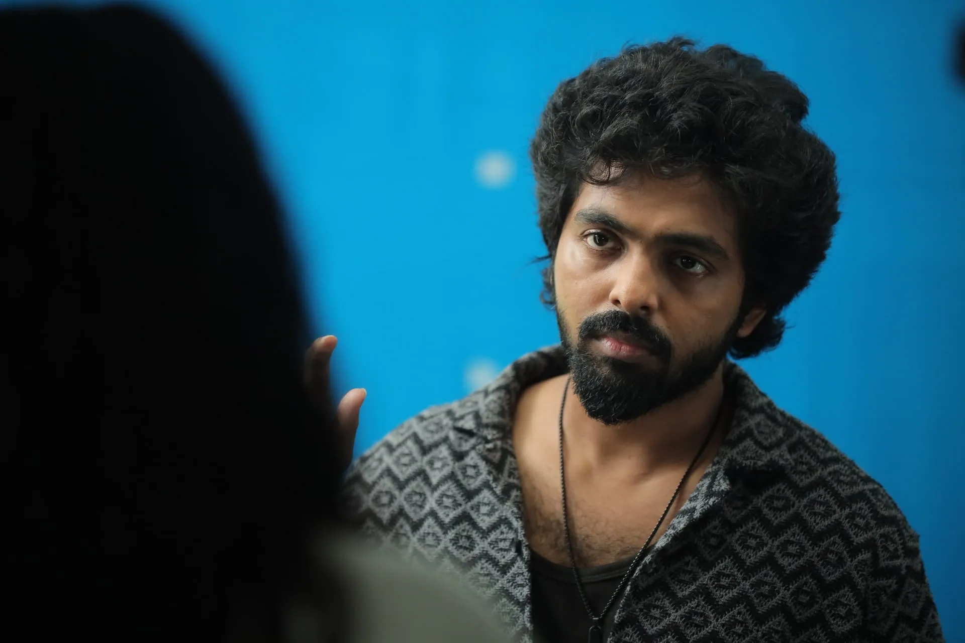 GV Prakash Kumar as Magi, tense and wary, against a blue wall in Immortal