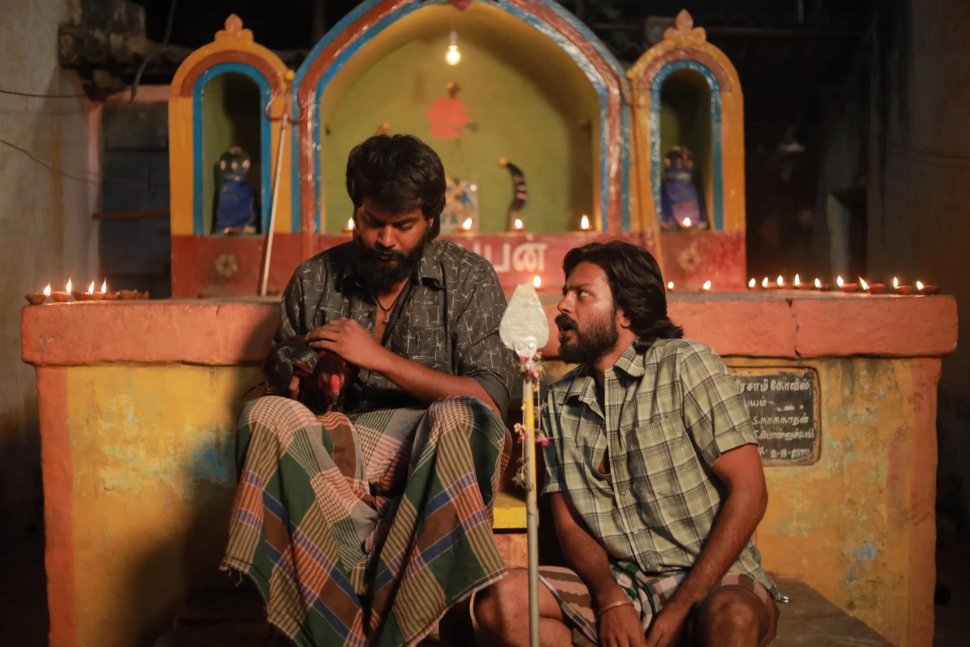 Karthi and Subbu share a quiet moment beside a shrine lit with lamps.