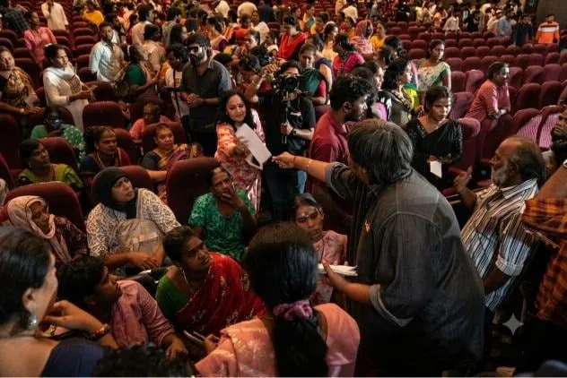 Karthik Subbaraj leans in to hand over a cheque in a packed theatre
