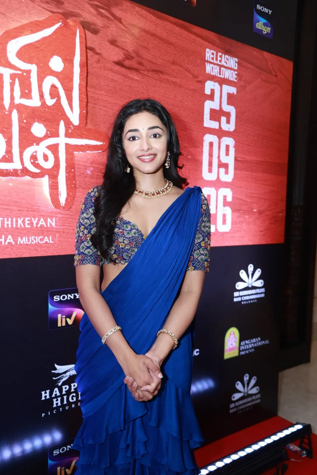 Portrait in a blue sari beside the Anbil Avan promotional display