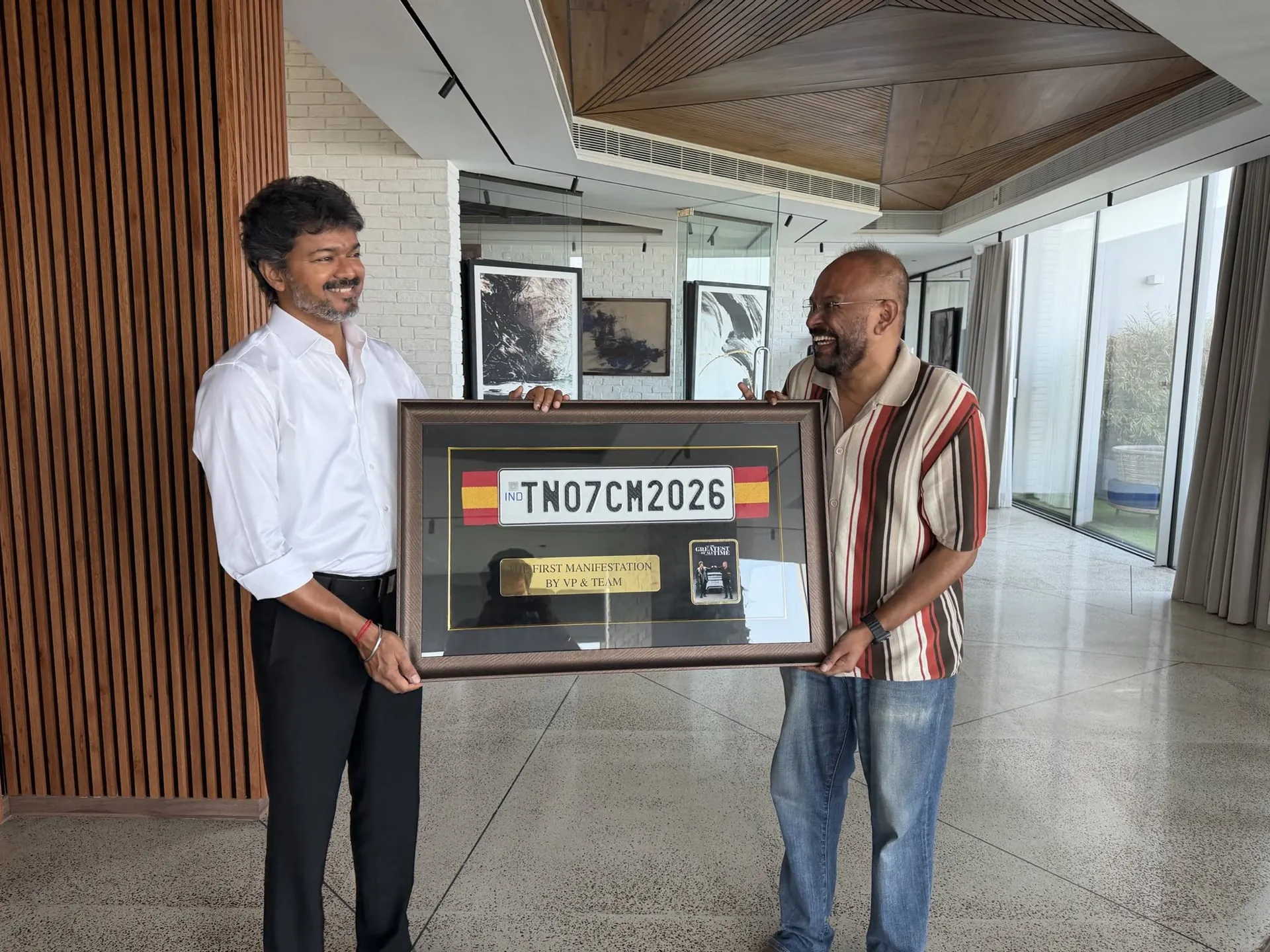 CM Vijay and Venkat Prabhu sharing a laugh while holding the framed plate between them in the chief minister's residence