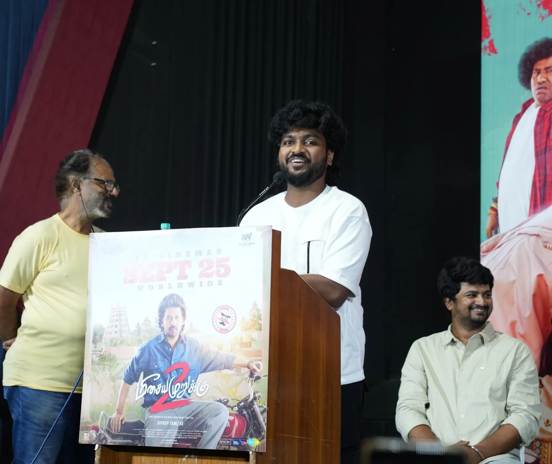 A smiling speaker in a white shirt addresses the Meesaya Murukku 2 audience
