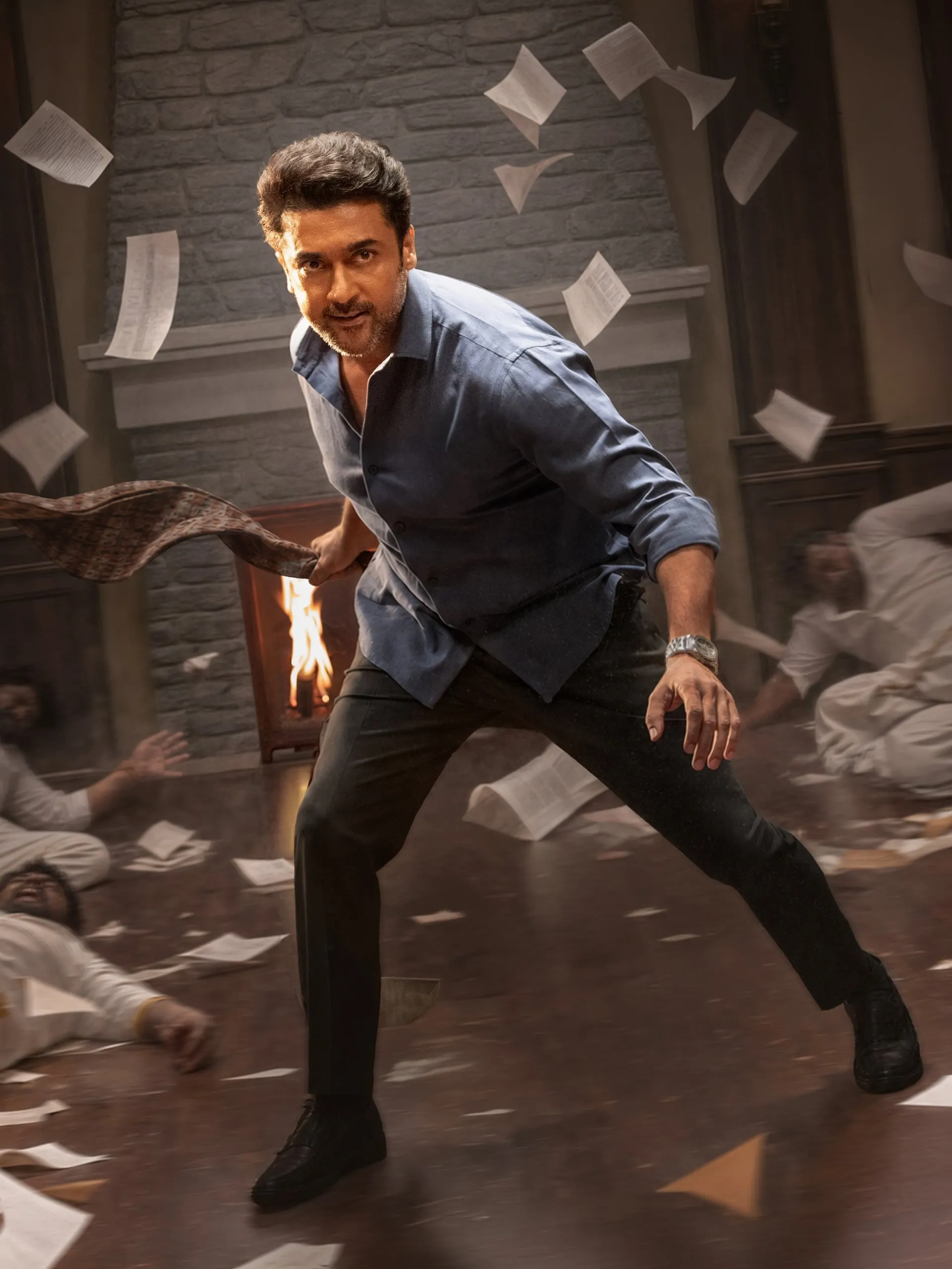 Suriya mid-stride in a chaotic room, papers flying around him