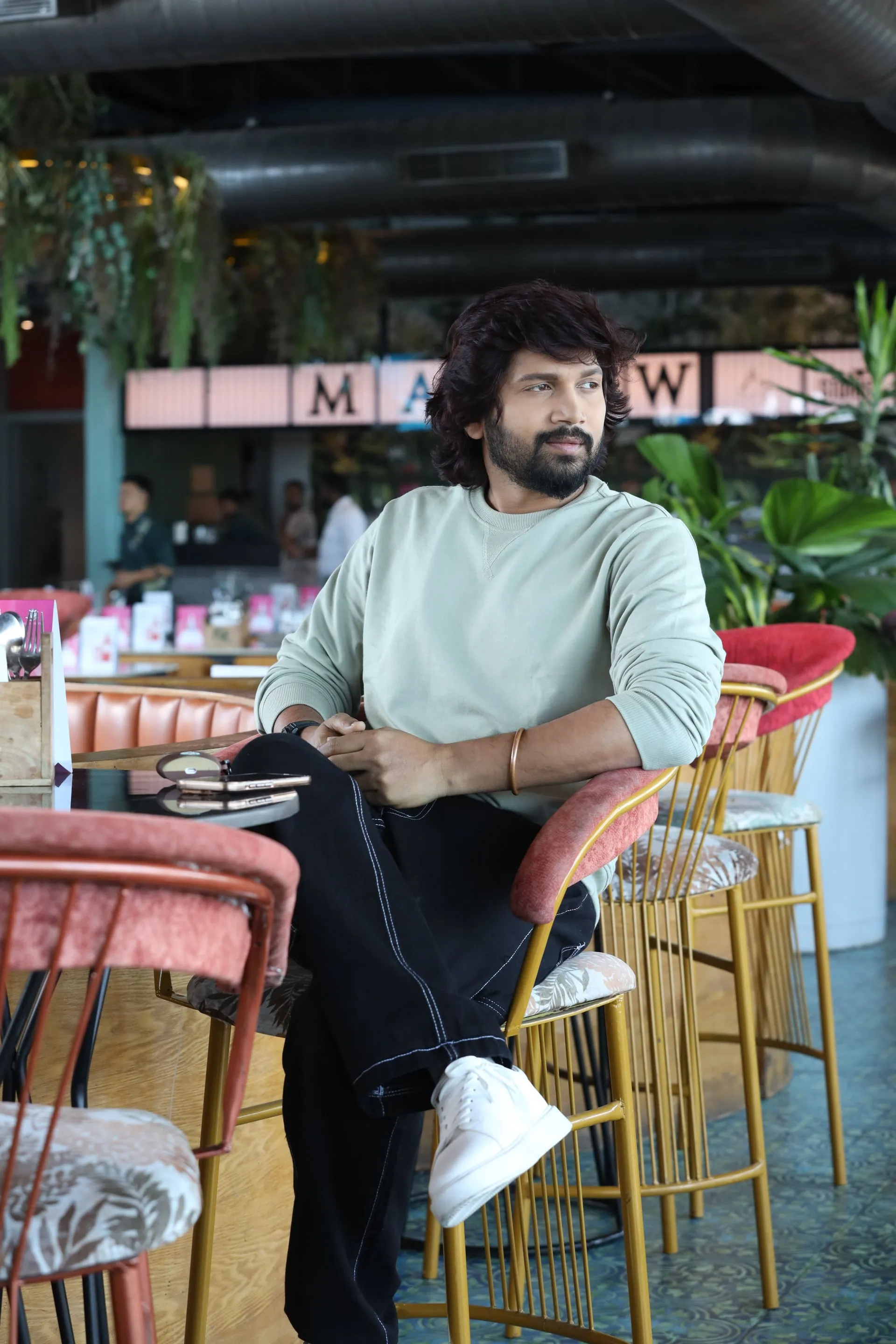 Vijay Vishwa seated at a cafe in a sage sweatshirt, hands clasped, looking into the camera
