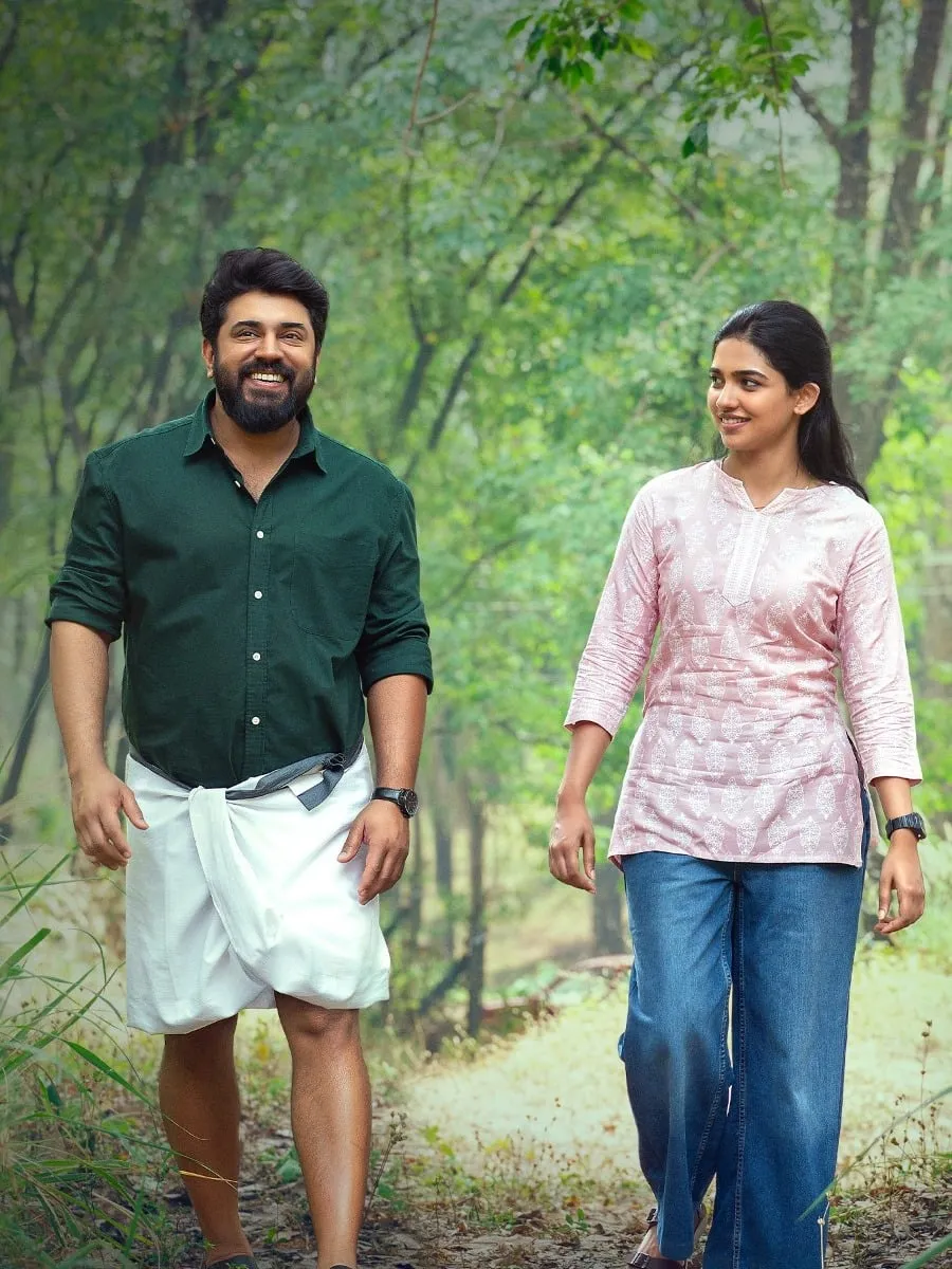 Justin in a dark green shirt and white mundu walks beside Ashley in a pink kurta and jeans along a tree-lined path in Bethlehem Kudumba Unit