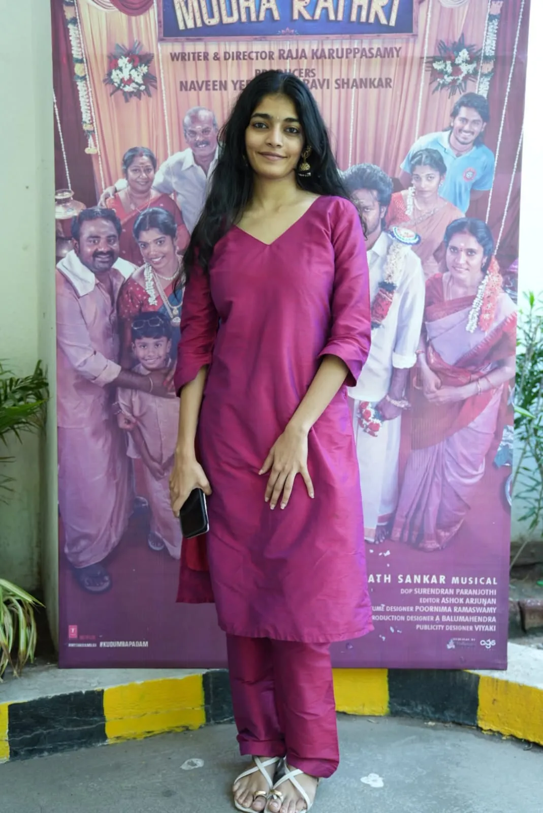 An attendee in a magenta outfit beside the film's ensemble poster at the thank-you gathering