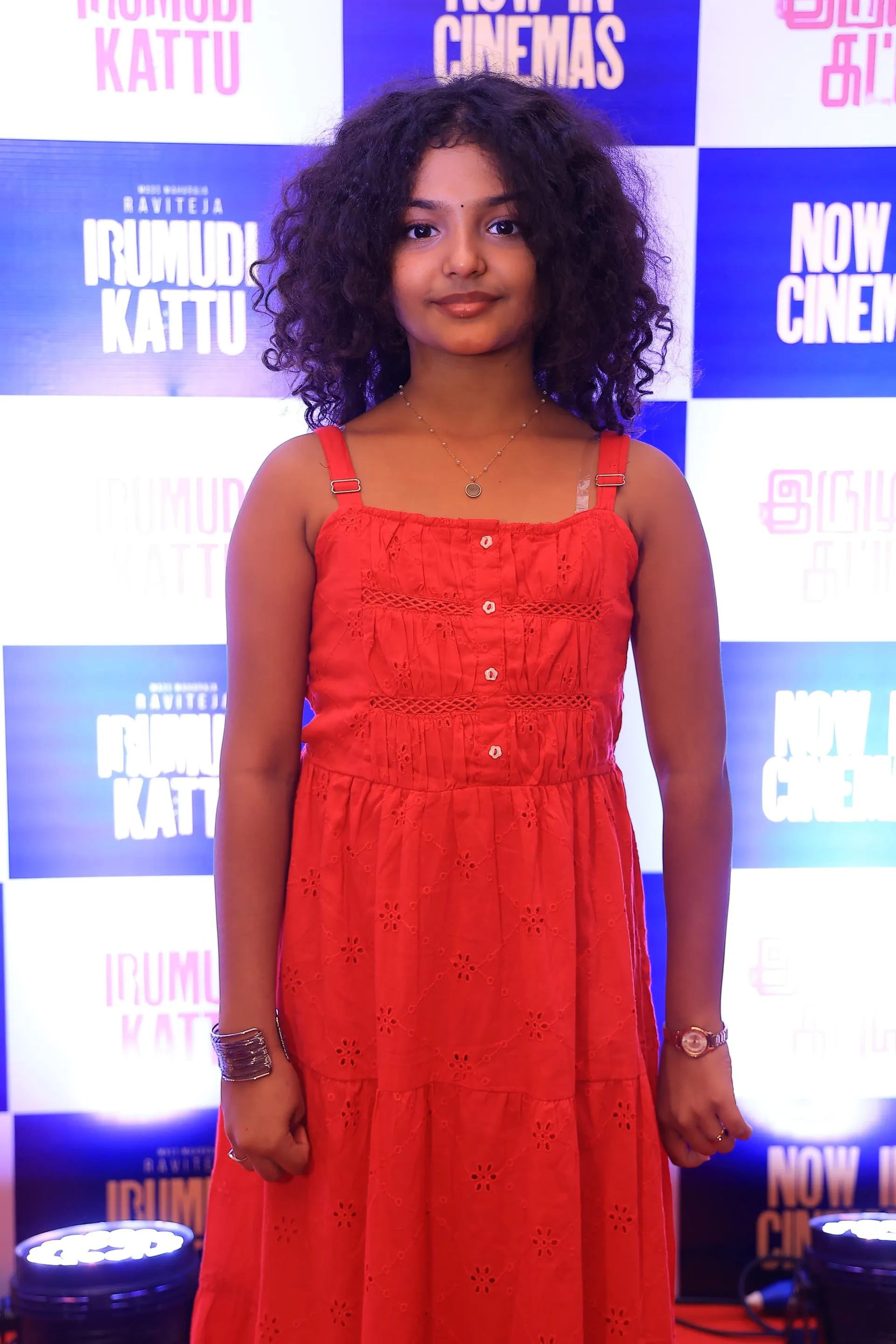 Baby Nakshathra in a red dress in front of the Irumudi Kattu poster wall