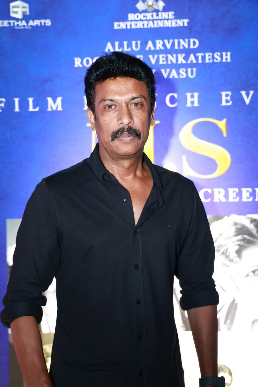 A guest in black poses before the M.S. film launch backdrop