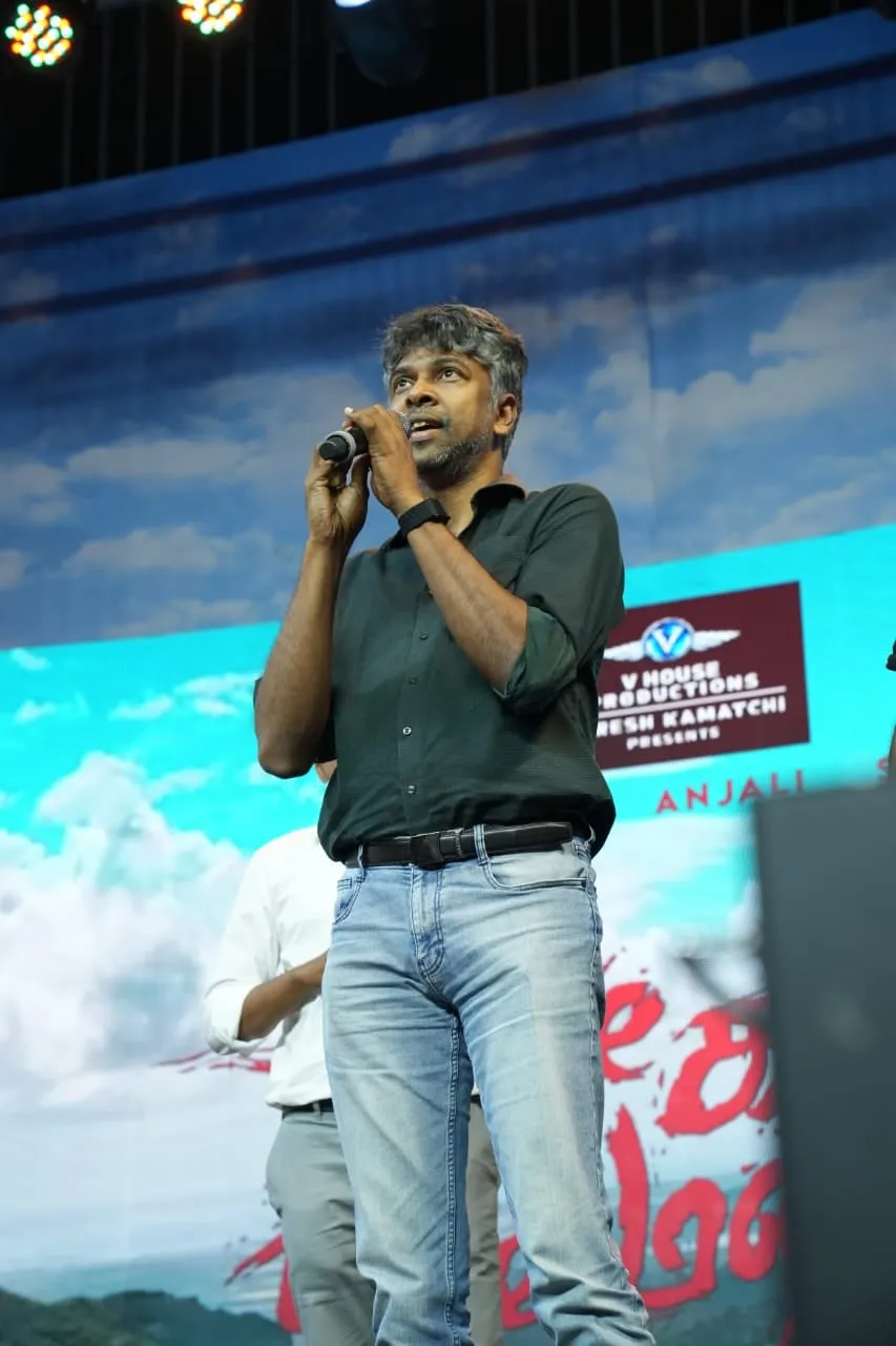 A speaker holds a microphone against the film's scenic stage backdrop