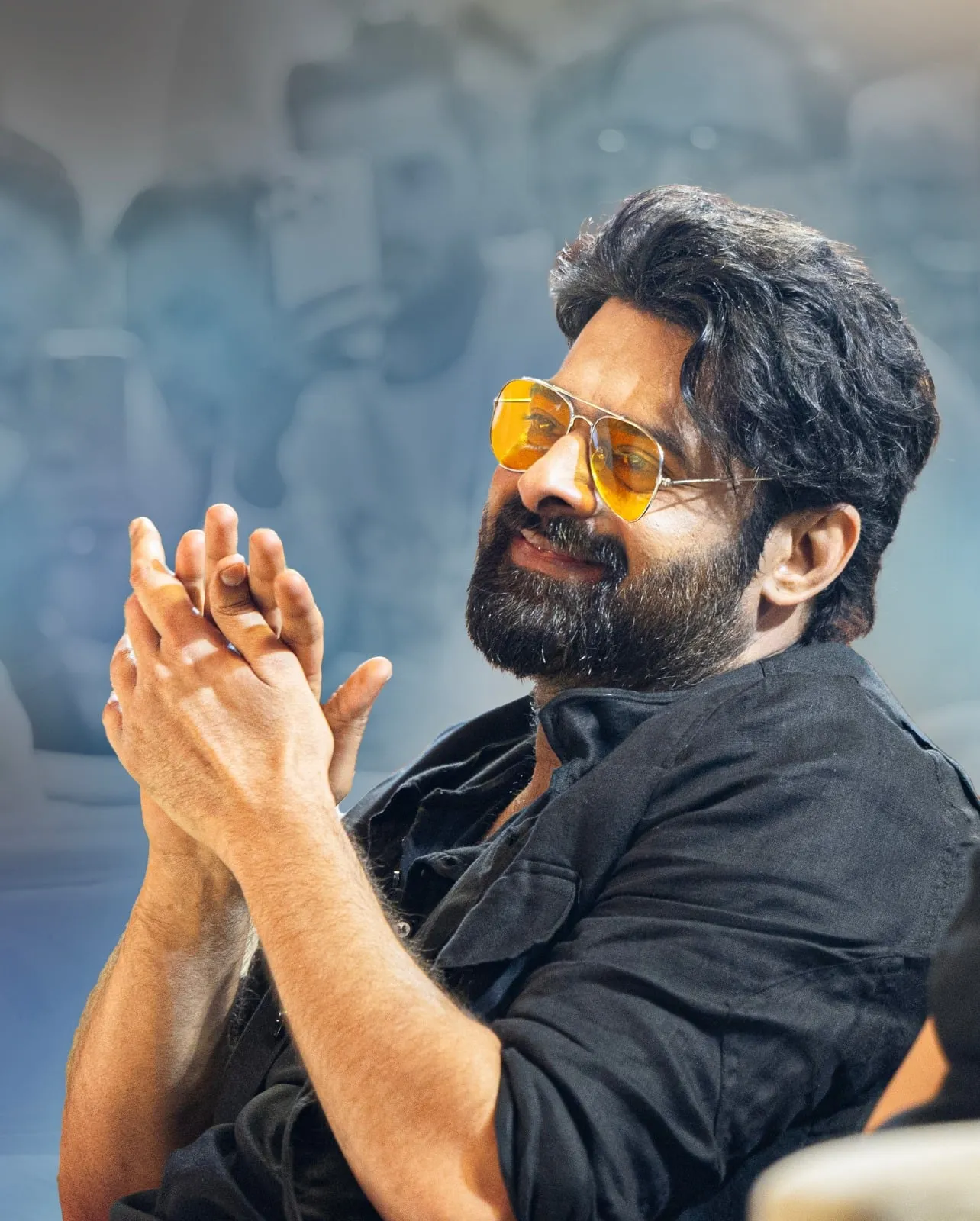 Prabhas seated with his hands together, wearing yellow-tinted glasses