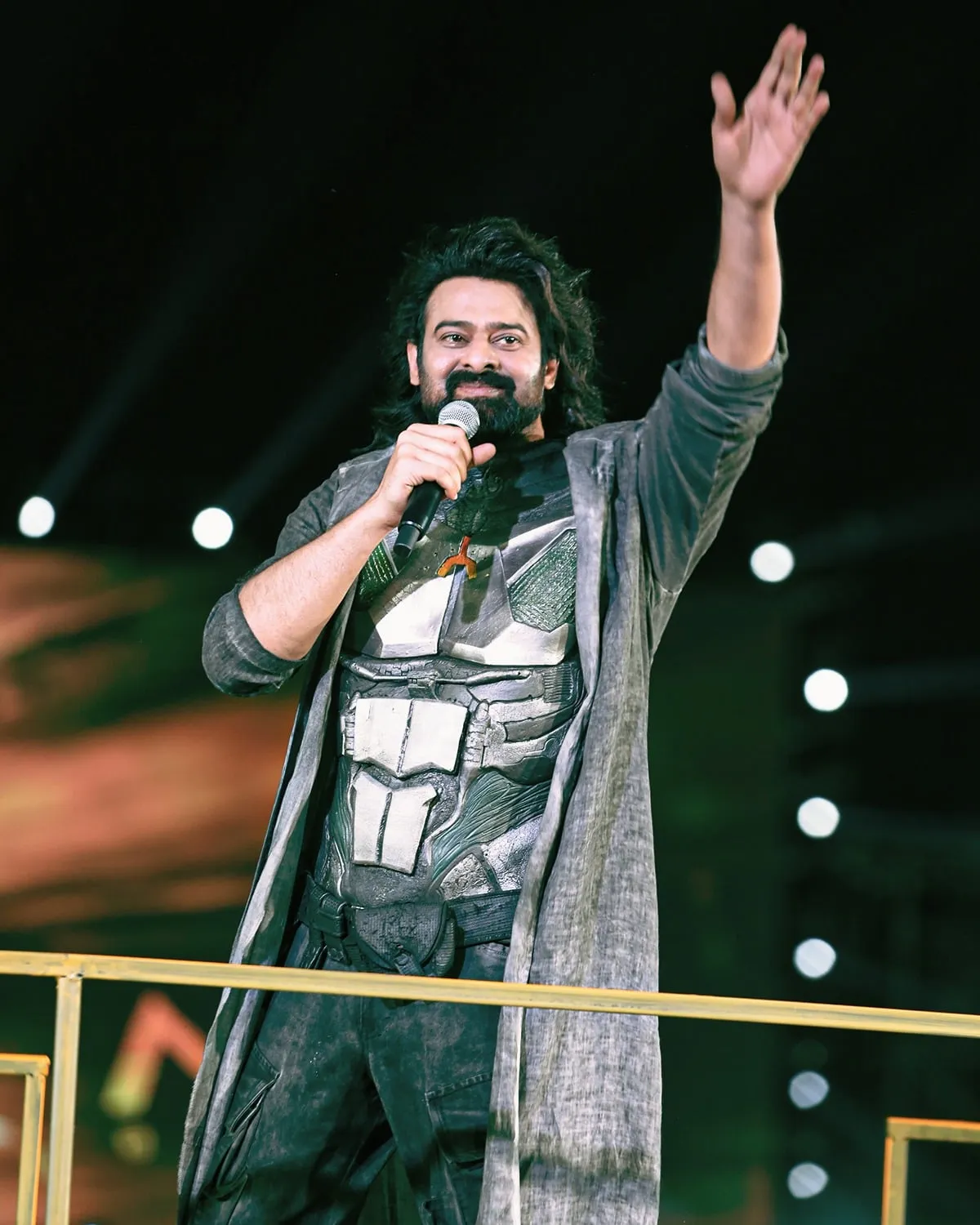 Prabhas waves to the audience while speaking into a microphone