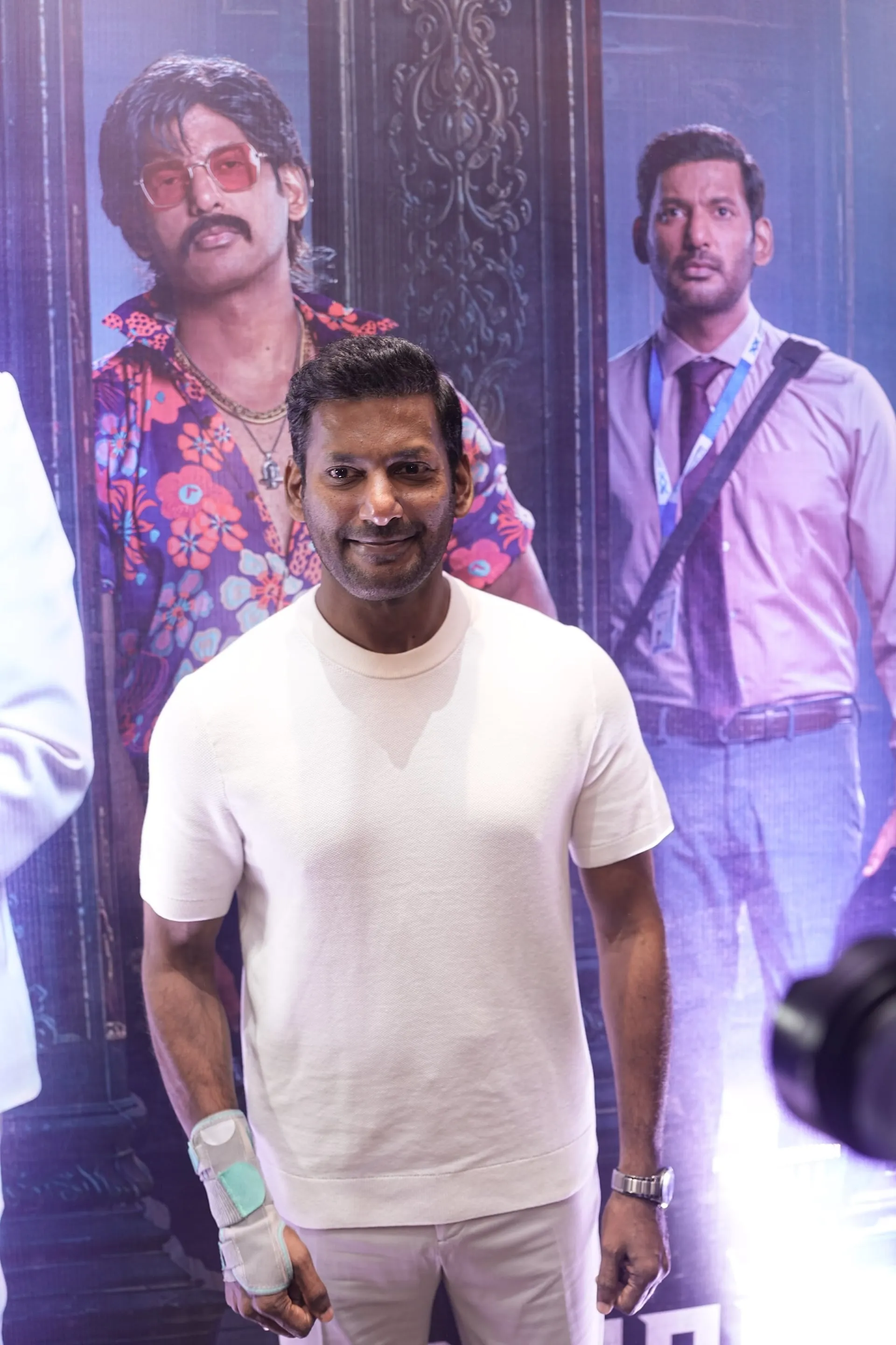 Vishal in white in front of the Magudam poster showing his gangster and corporate looks